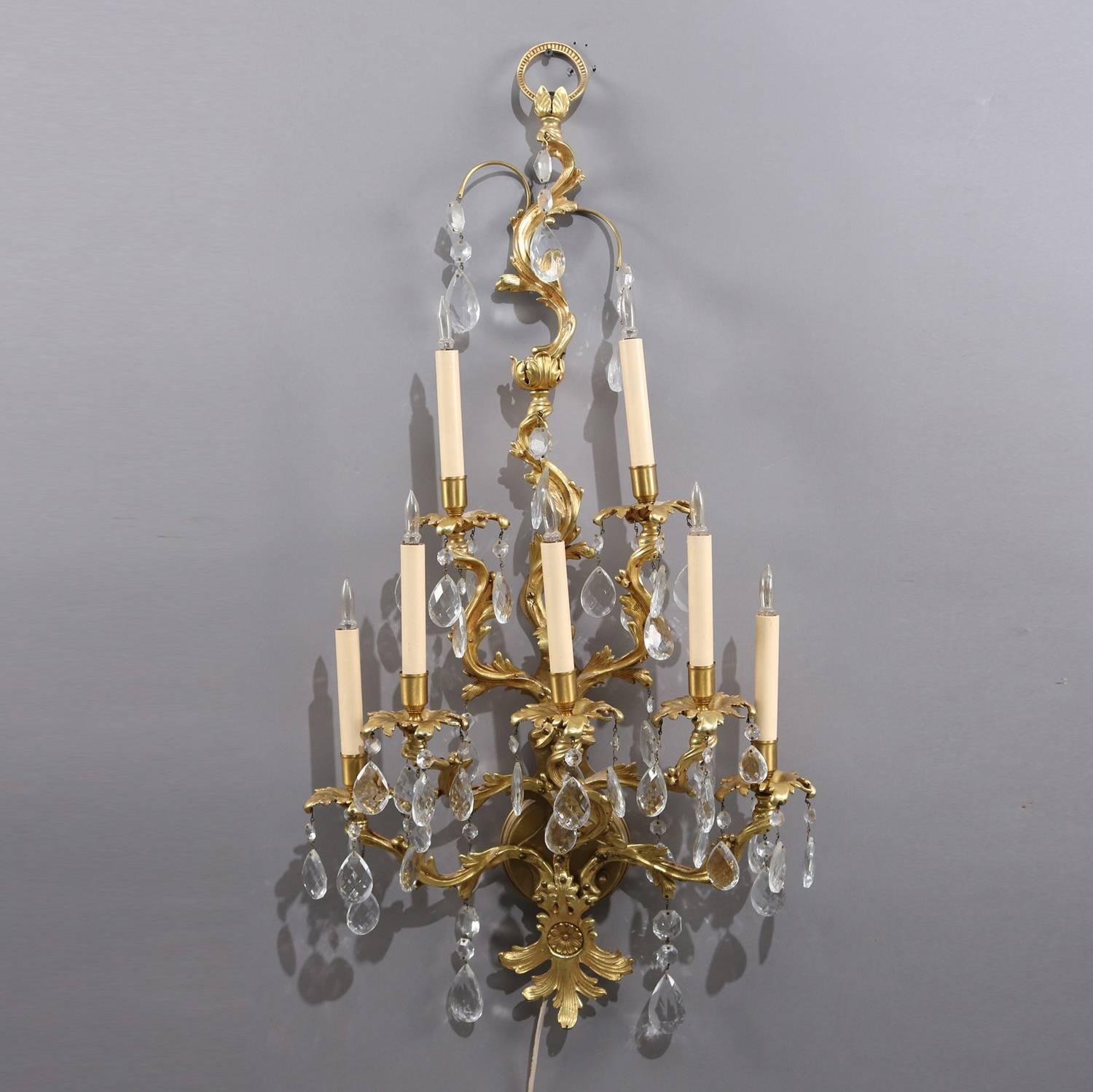 Oversized pair of French Rococo gilt wall sconces feature gilt bronze in foliate form with palmette apron and seven candle lights with overall hanging cut crystals, electric having plugs and switches, circa 1940.

Measures: 42
