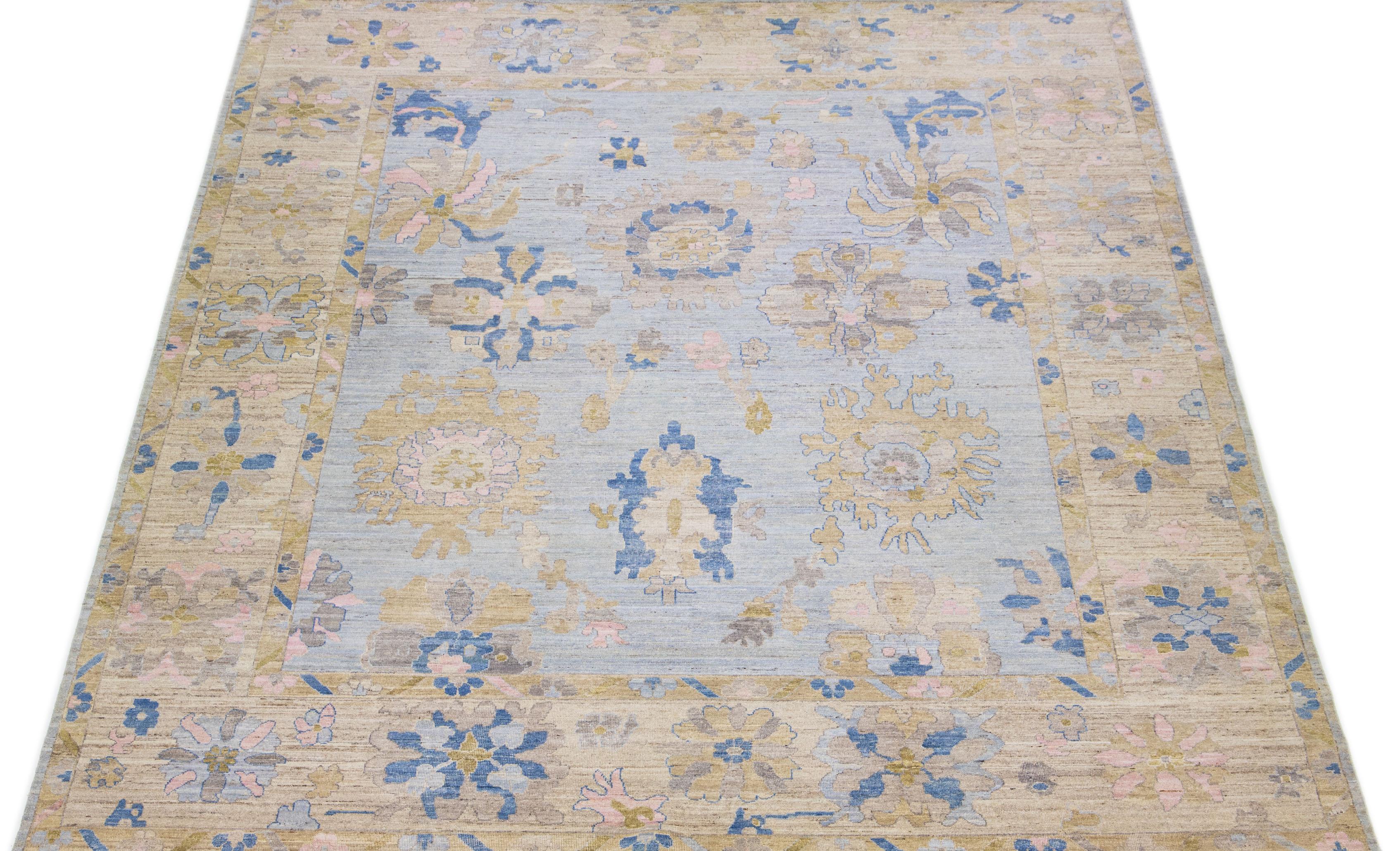This contemporary Oversize Oushak Style rug boasts a hand-knotted wool construction, complemented by a charming light blue color. Its tastefully crafted frame showcases lovely floral motifs in a fascinating blend of brown, pink, and blue