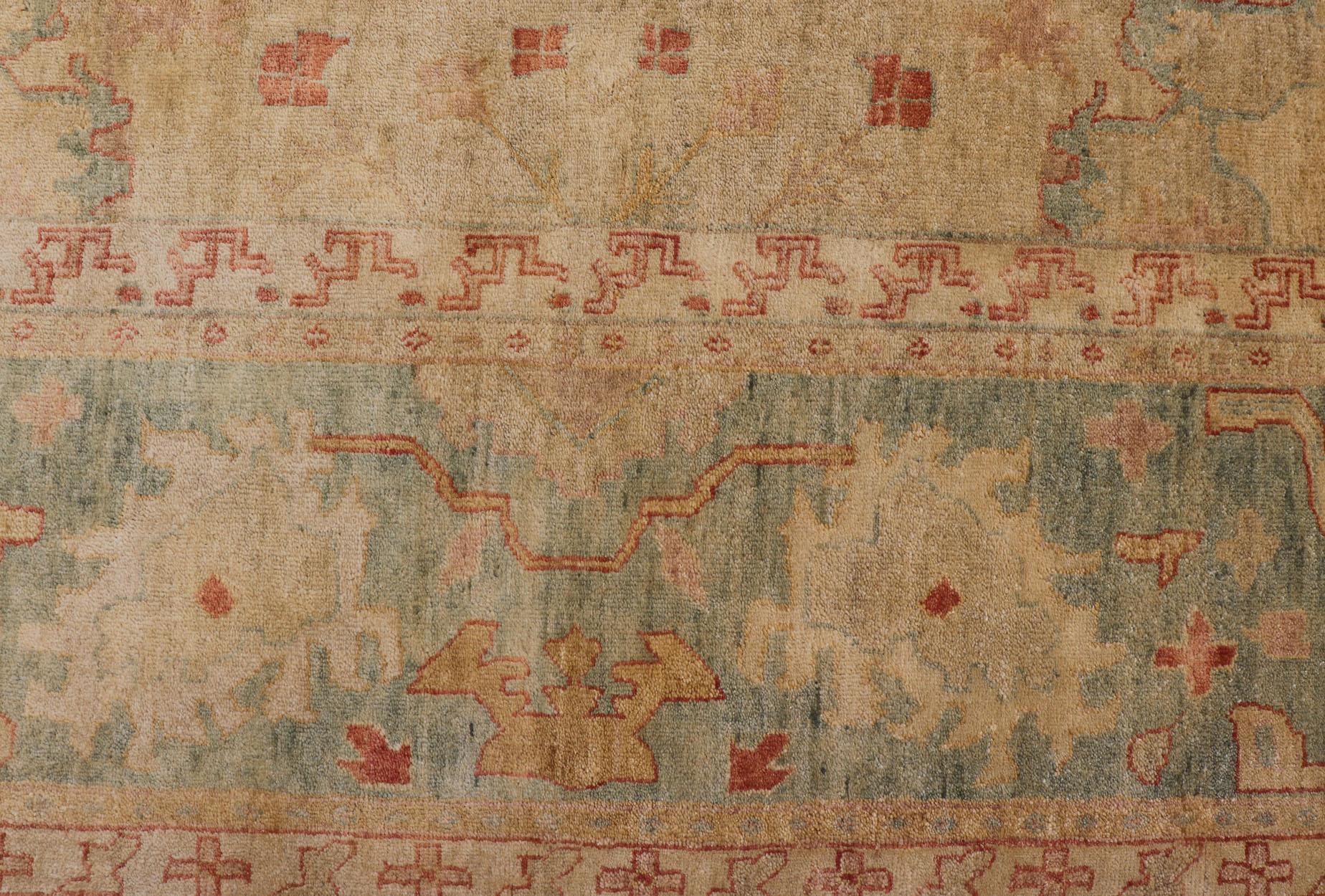 Oversized Hand-Knotted Tribal Diamond Oushak in Tan and Green Tones.
 Measures 10'3 x 14'3
This woven art was hand-knotted in India during the 2010's. This wide banded border is rendered in a blue green, holding a common leaflet repeating design.