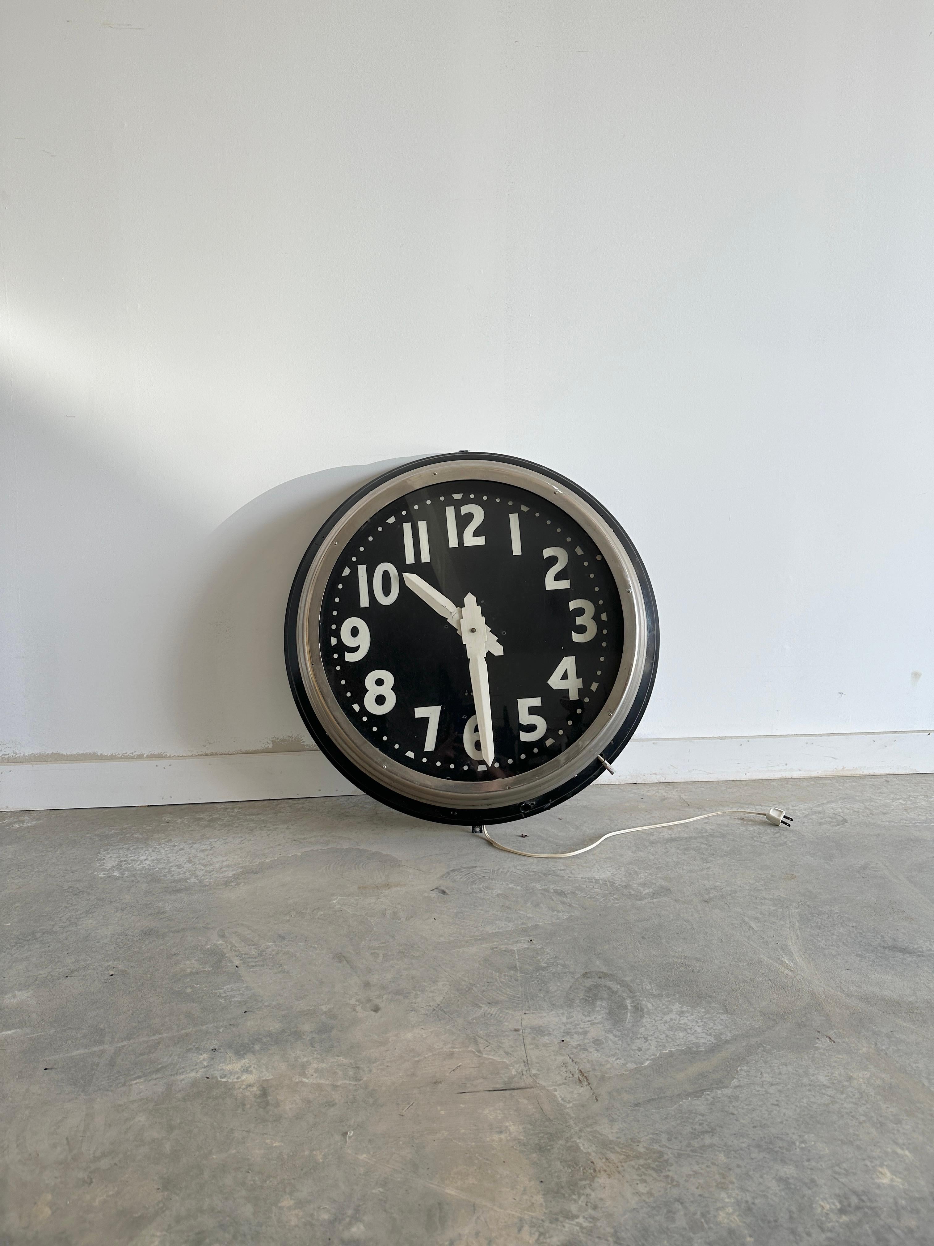 Large light up wall clock with handpainted numbers in metal and black wood frame. Good working condition with moderate patina throughout.