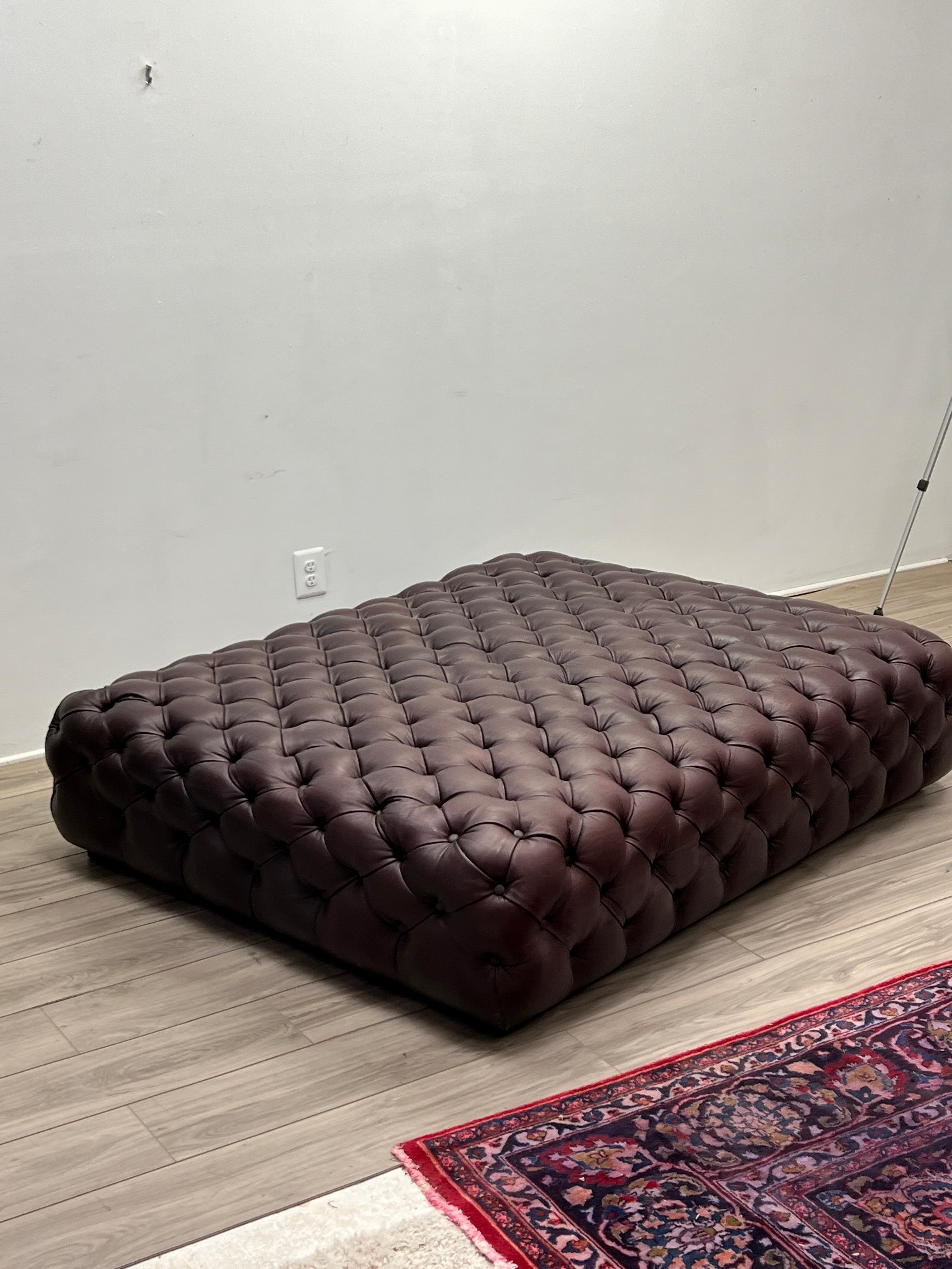 Featuring a unique and stylish low profile oversized Chesterfield ottoman with supple Burgundy leather. A well made and comfortable ottoman in good condition. All of the buttons are tight and intact. The rich leather is in good condition with no