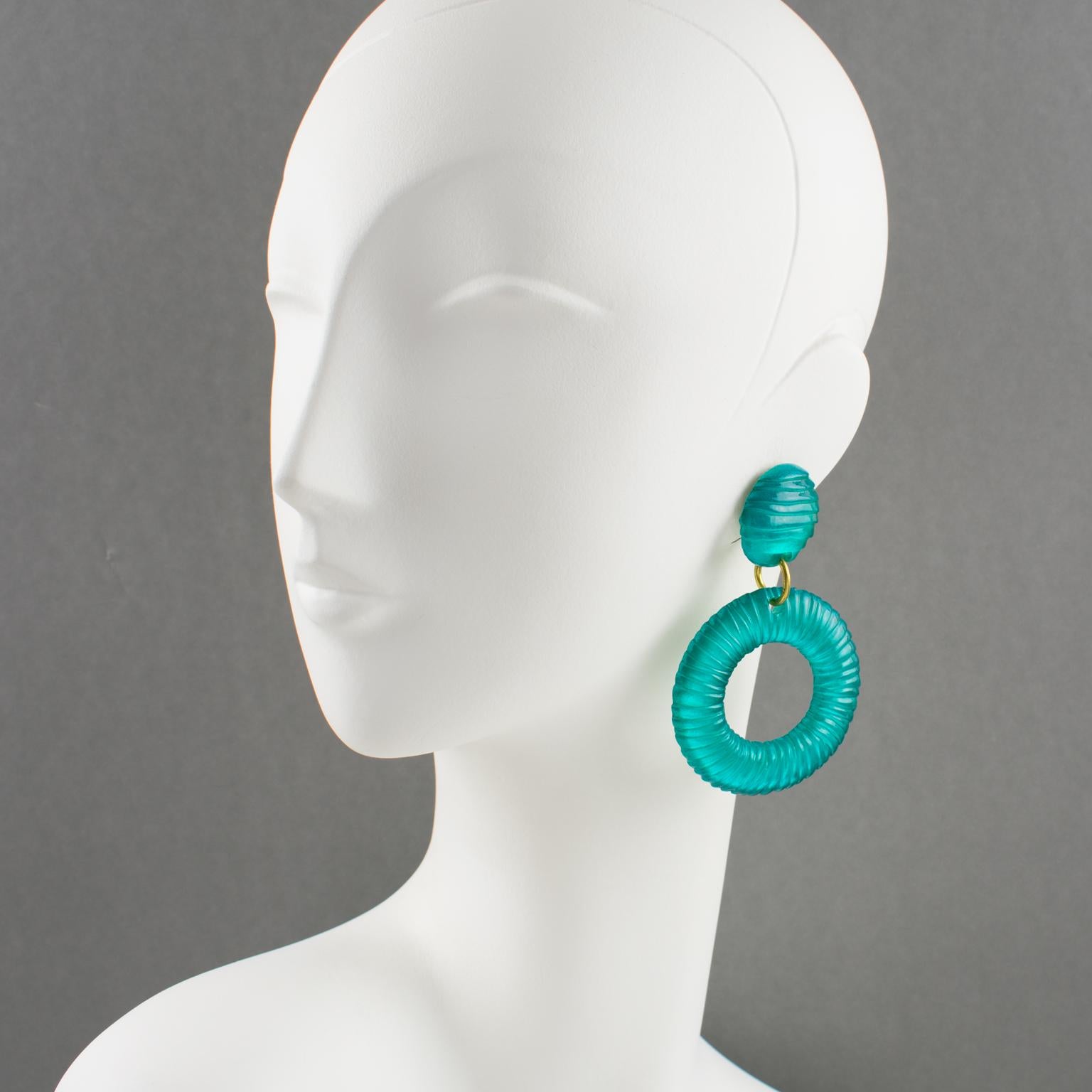 Lovely bright blue oversized lucite clip-on earrings. Large donut hoop dangling shape with a striped carved textured pattern. A bright aqua turquoise blue color on metallic gray background.
Measurements: 3.19 in. long (8 cm) x 2.13 in. wide (5.3 cm)