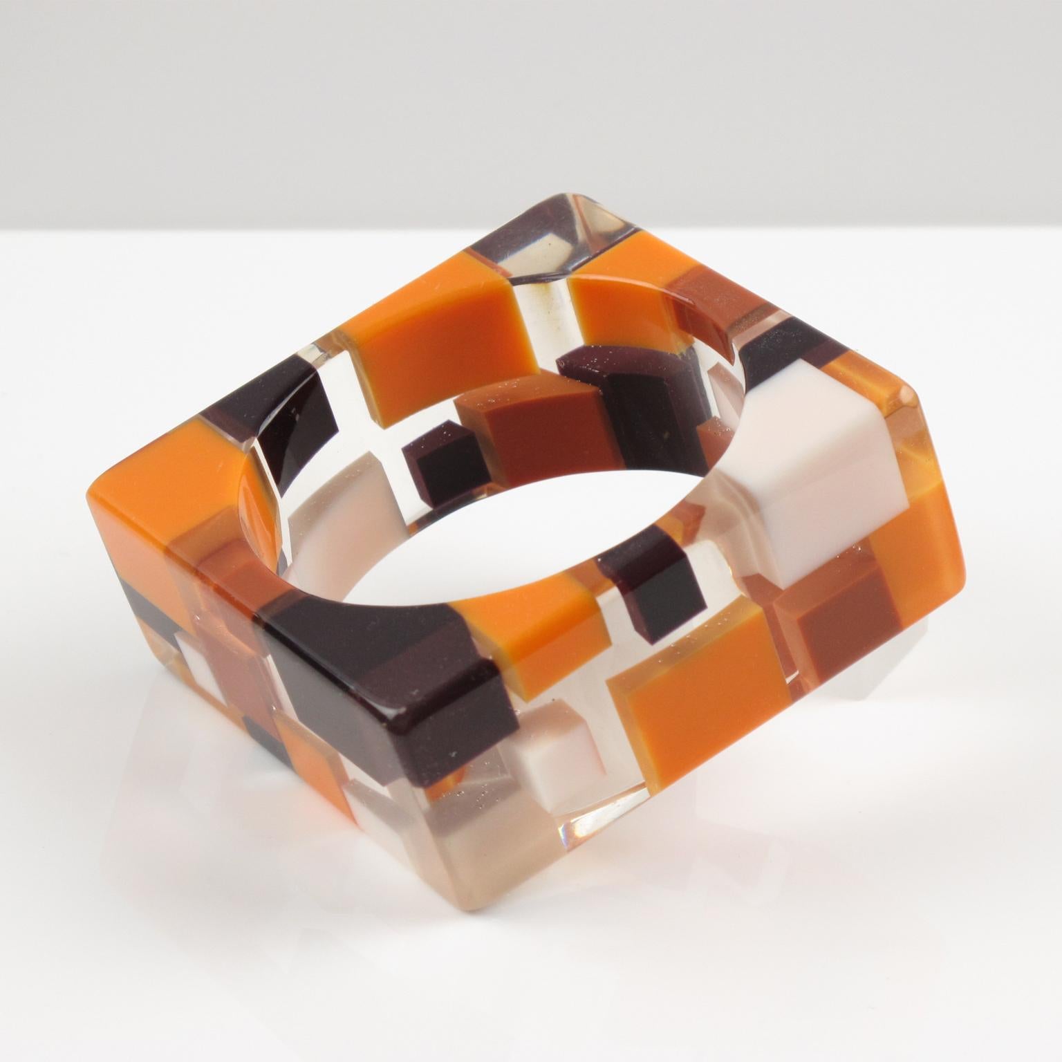 Lovely chunky extra wide geometric Lucite bracelet bangle. Oversized square carved shape with colorful checkerboard inclusions. Build on a crystal clear background with imbedded geometric elements in assorted colors of orange, brown, white and