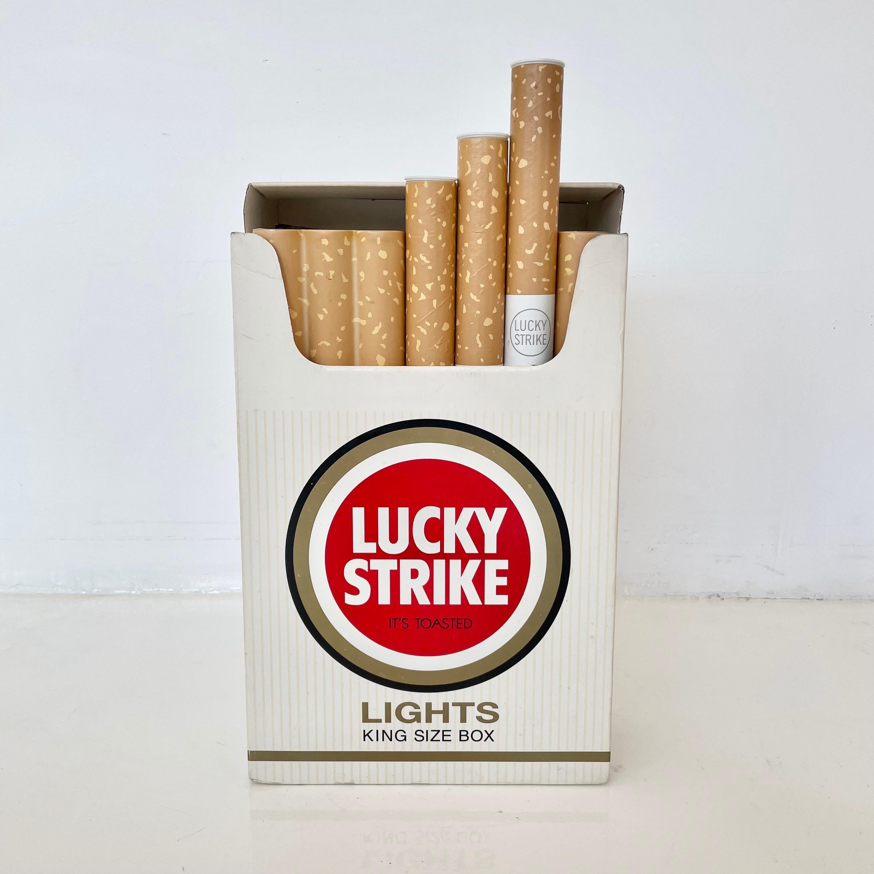 Cool oversized store display of Lucky Cigarettes. Cardboard Lucky Strike cigarette pack. Box opens. Three cigarettes pull out. Made of paper, plastic and cardboard. Fun piece of pop-art. Good condition with some wear.