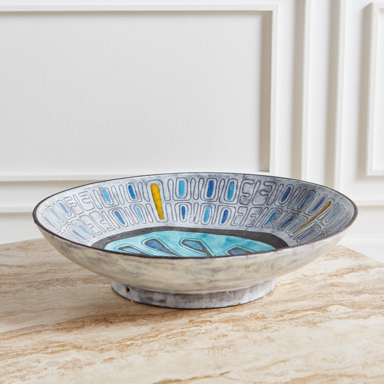 A textural oversized Mid Century glazed Ceramic bowl featuring a primitive design and vibrant blue and yellow hues. Marked S227 on underside. This bowl can sit on a table top or hang on the wall. Hanging hardware not included.