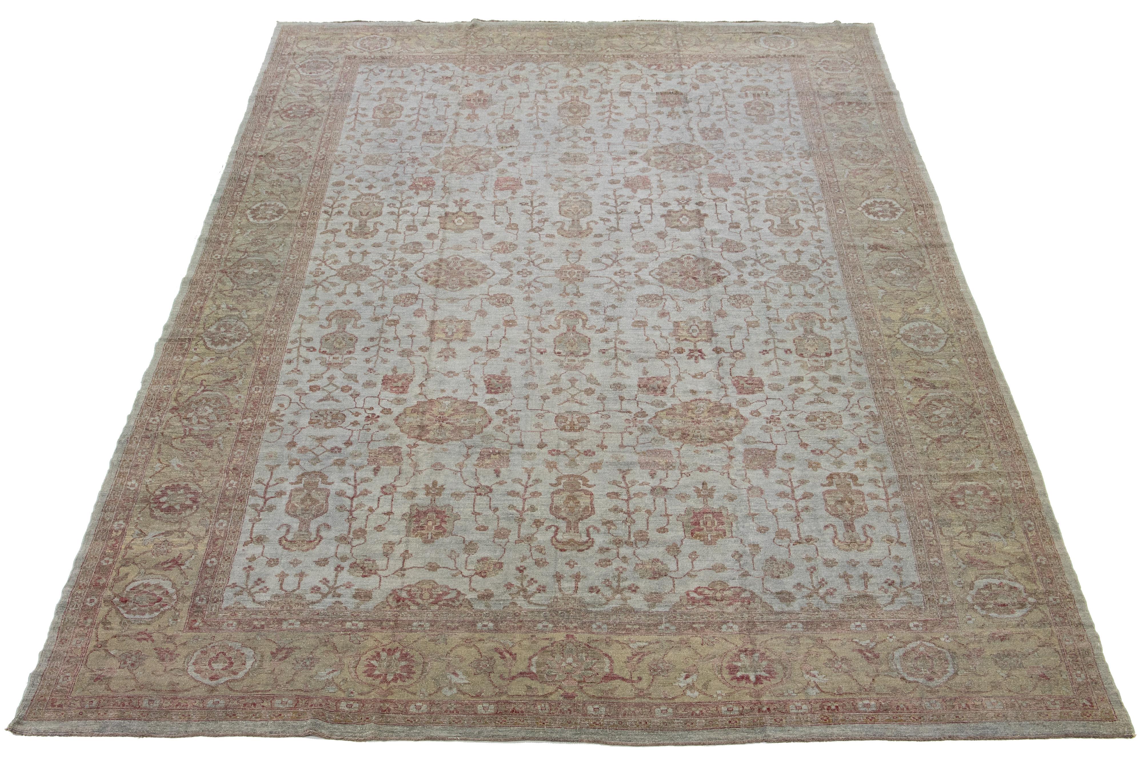 Dieser Wollteppich mit moderner Ästhetik zeigt ein Design im Oushak-Stil. Sein graues, handgeknüpftes Feld ist hellbraun umrandet und mit lebhaften Blumenmustern verziert, die sich über den gesamten Teppich erstrecken.

Dieser Teppich misst 12' x