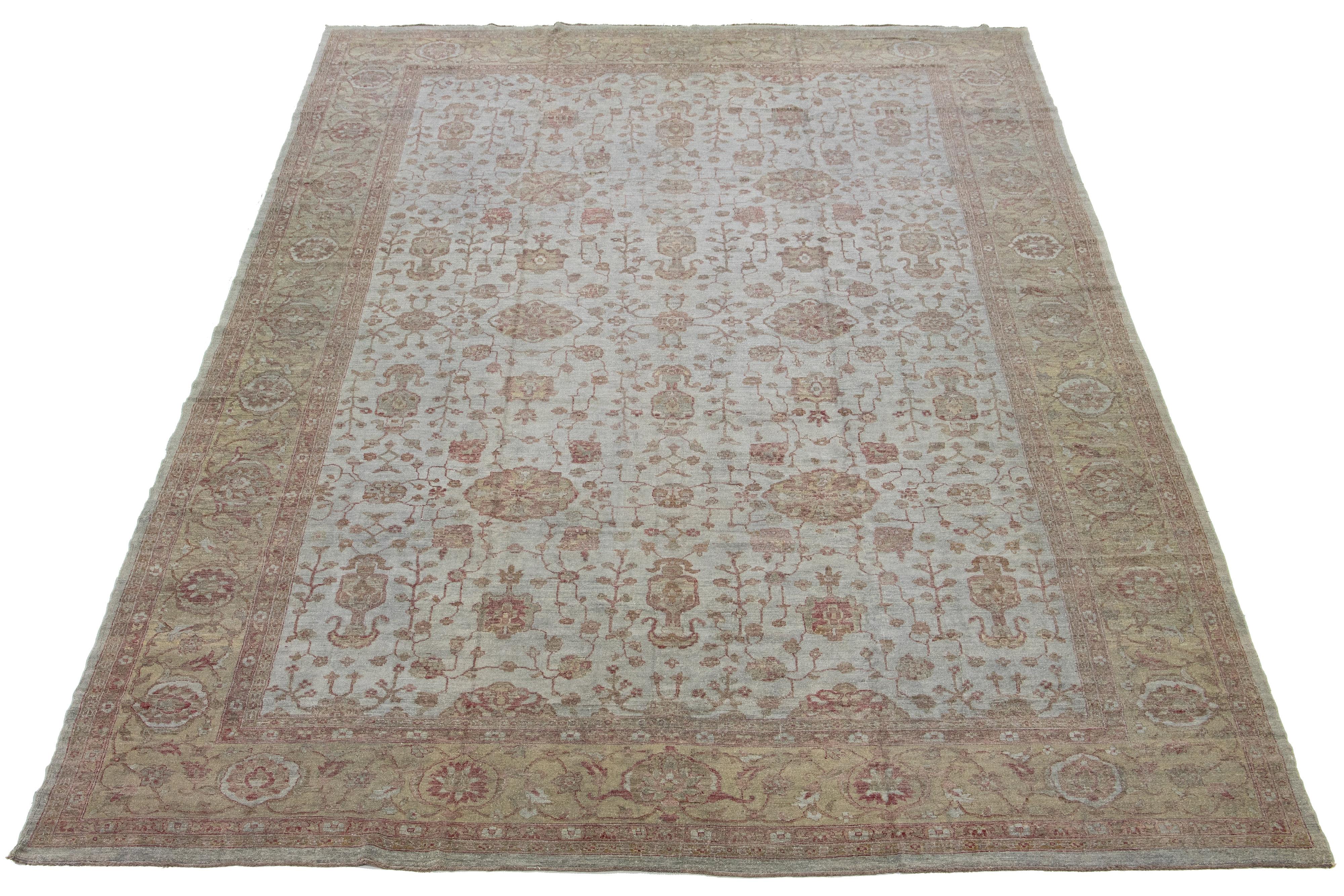 Featuring a modern aesthetic, this wool rug displays an Oushak-style design. Its gray hand-knotted field is bordered with tan and adorned with vibrant floral patterns that extend across the rug.

This rug measures 12' x 18'1