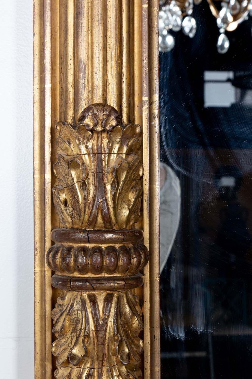Un joli miroir au cadre doré, évoquant la grâce de l'ère néoclassique, fabriqué en Angleterre au début du XXe siècle. D'une taille impressionnante, il est doté d'une plaque de miroir originale, reflétant la grandeur de l'époque. Ornées de délicats