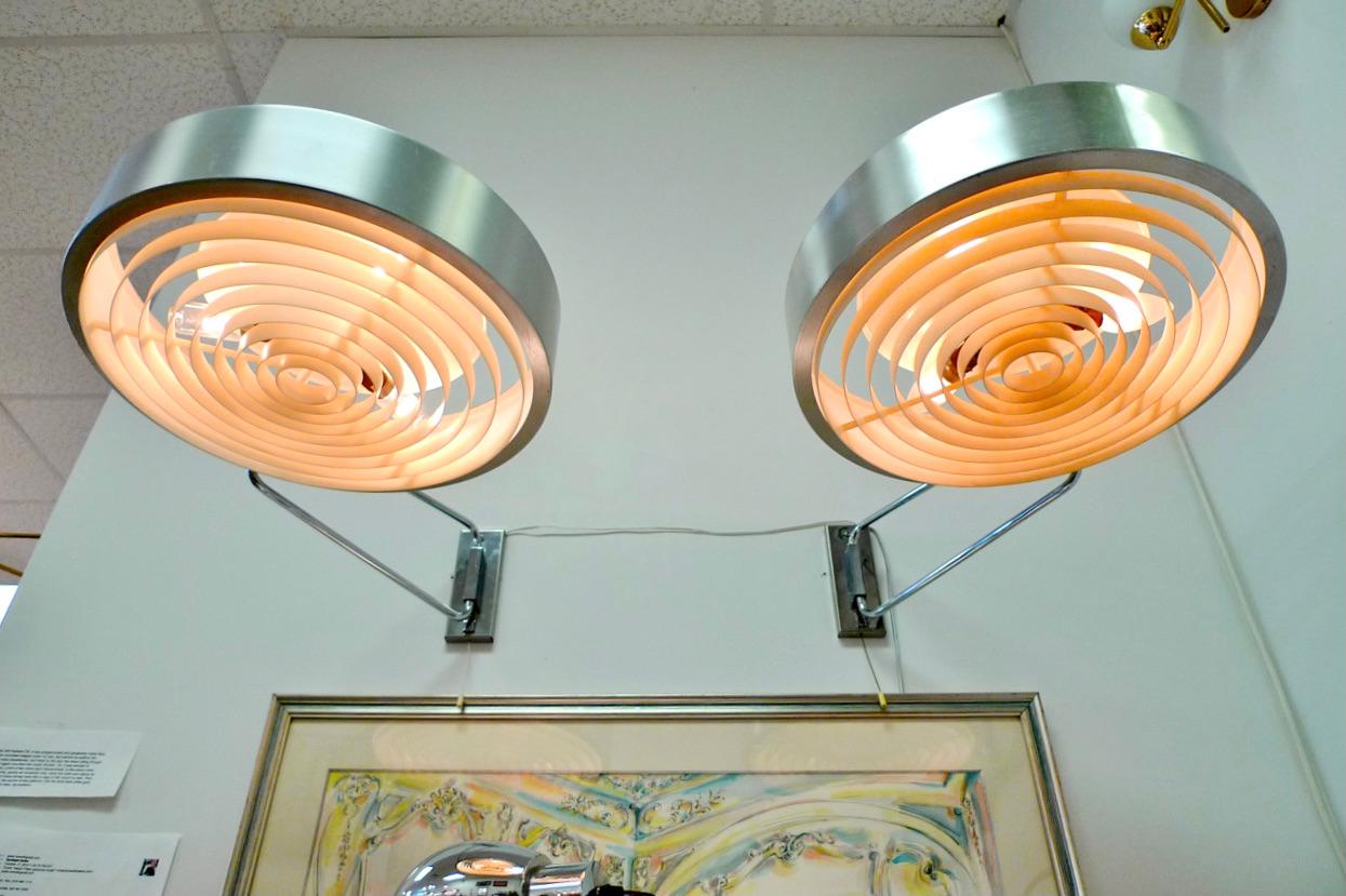 Unusual and oversized pair of French swing arm wall lights.  Bracket and head move independently.  Concentric circles plastic diffusor.
They extend from the wall up to 30.5 inches.
The stainless steel light head is 15.75 inches diameter and 5 inches