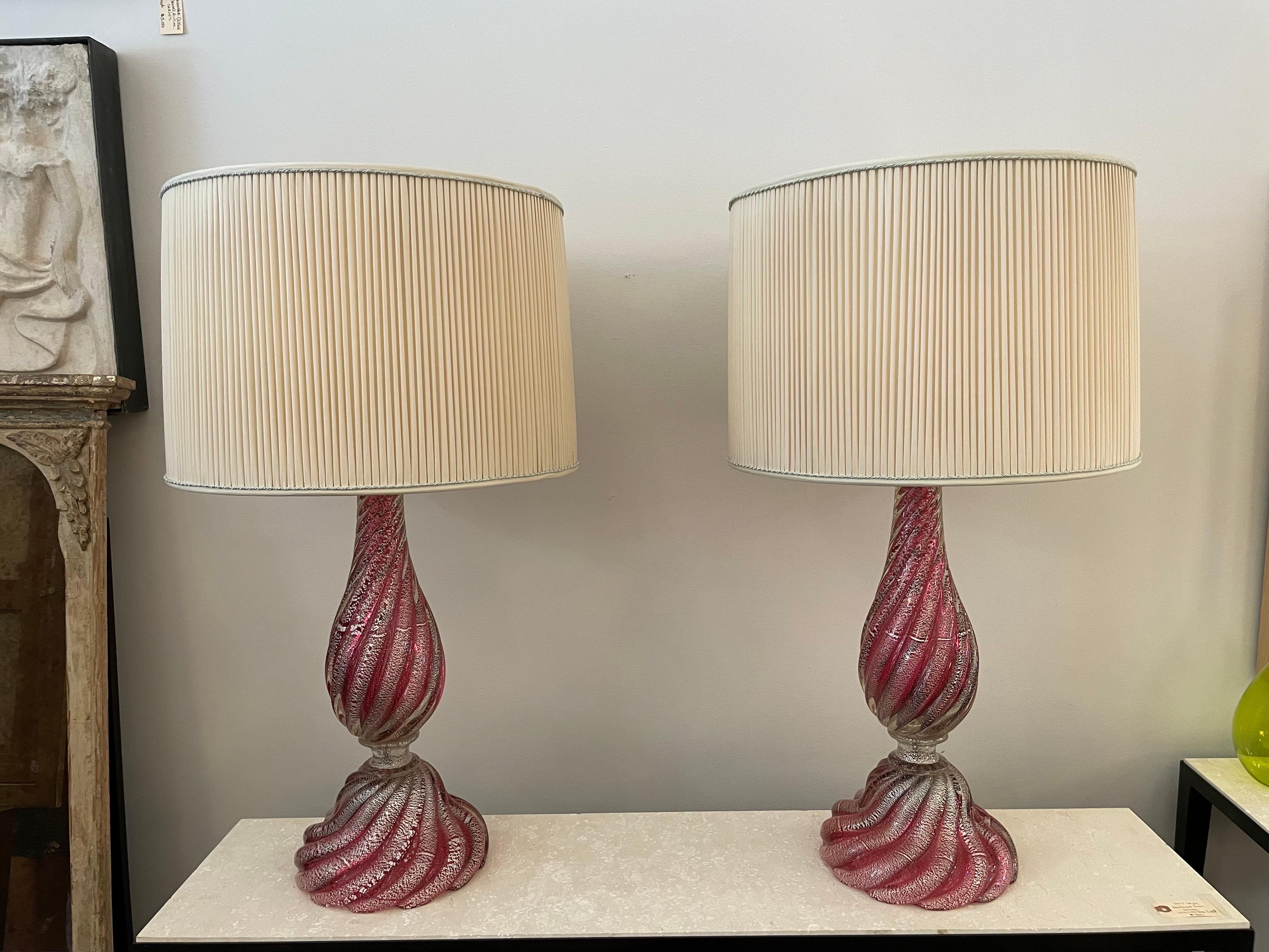 Il s'agit d'une élégante paire de lampes en verre de Murano de couleur framboise avec des inclusions de feuilles d'argent. Magnifique base et corps tourbillonnants - illuminés ou non, ils font une déclaration étonnante. Les abat-jour plissés