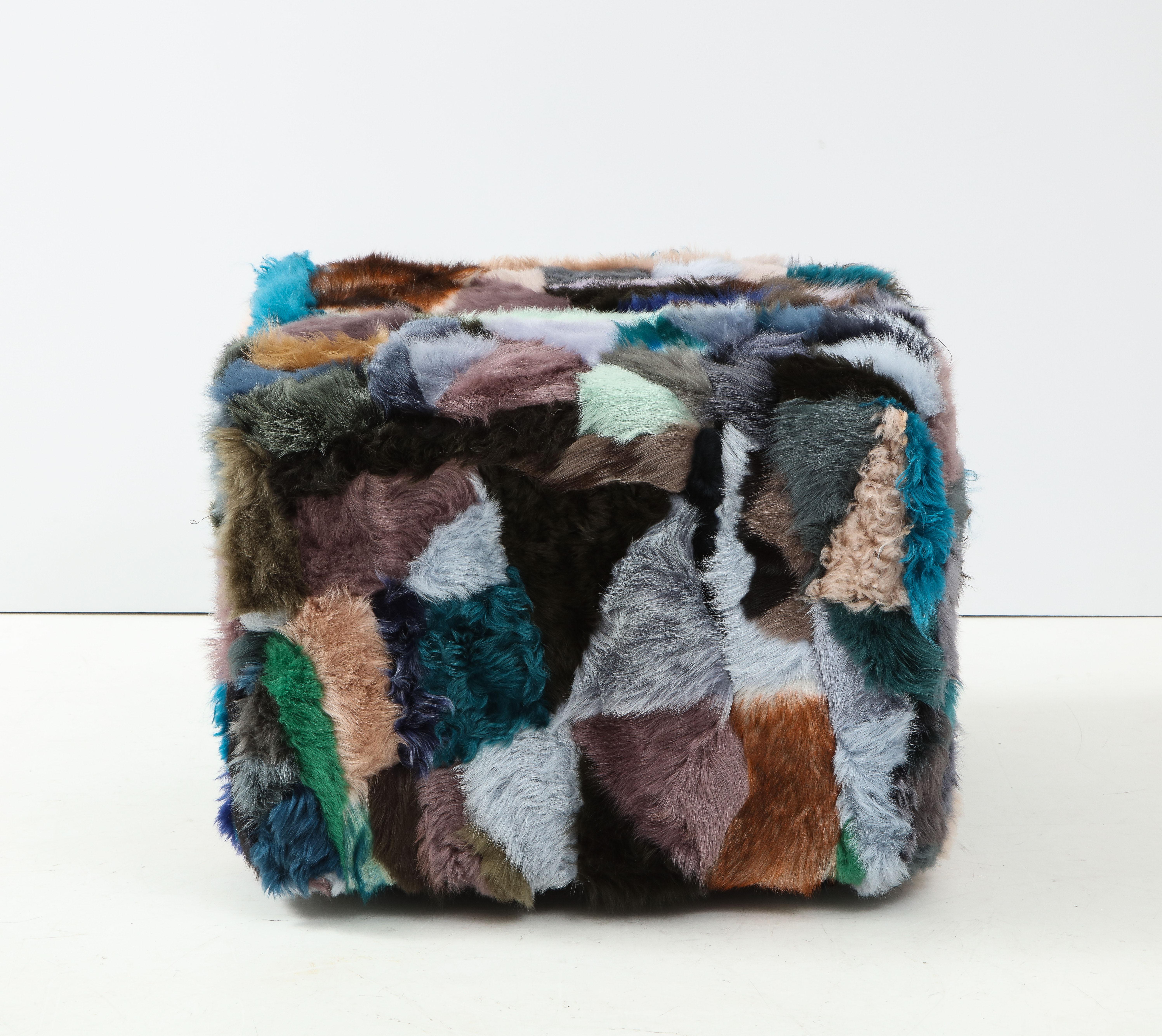 Fendi inspired cube ottoman upoholstered in patchwork Australian sheepskin in varying colors and thickness. Ottoman is on 4 tapering wood legs. A cozy seat in any setting.