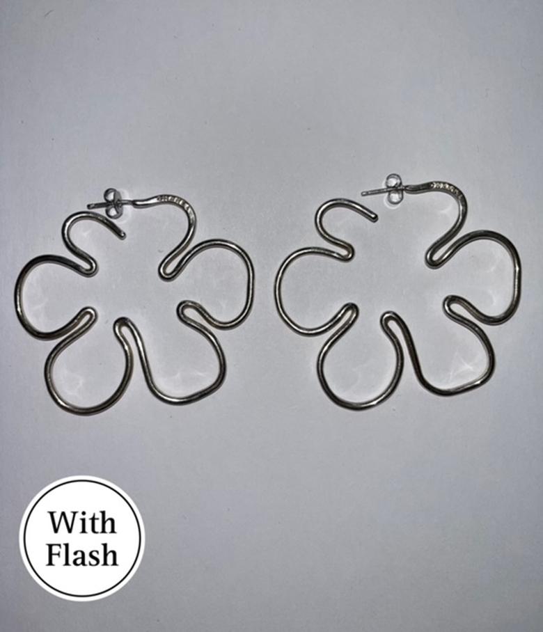 These striking earrings by Chanel blend sculptural elegance with a contemporary edge. Crafted in a lustrous silver-toned finish, the design features an abstract, flower-inspired silhouette in a refined hoop style. Anchored by a discreet stud