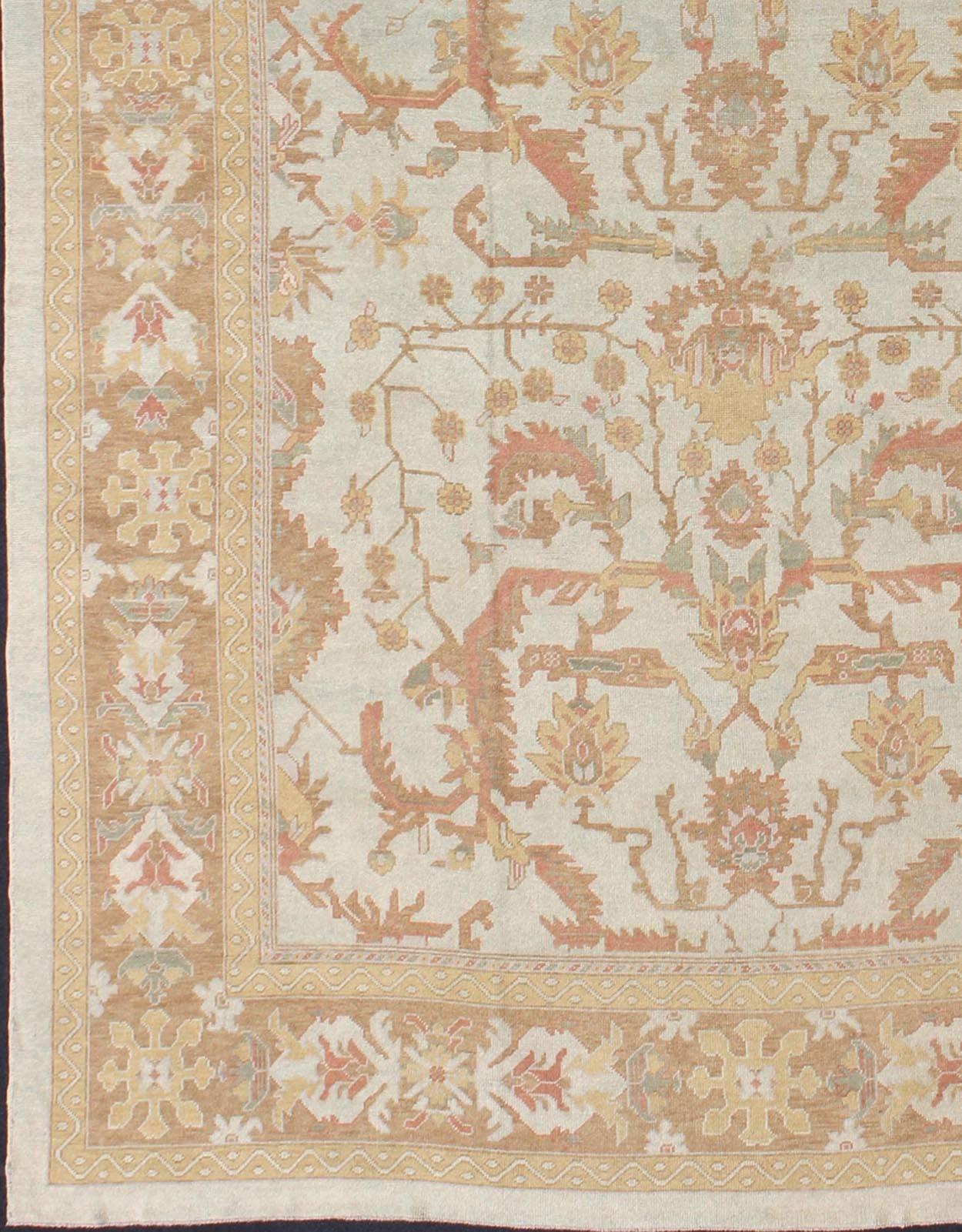 This Oushak rug was hand knotted in Turkey. This woven art boasts a unique color palette, featuring silver tone background, cream light blue, soft terra cotta,  green, light brown and yellow tones, . The border displays repeating arts & crafts