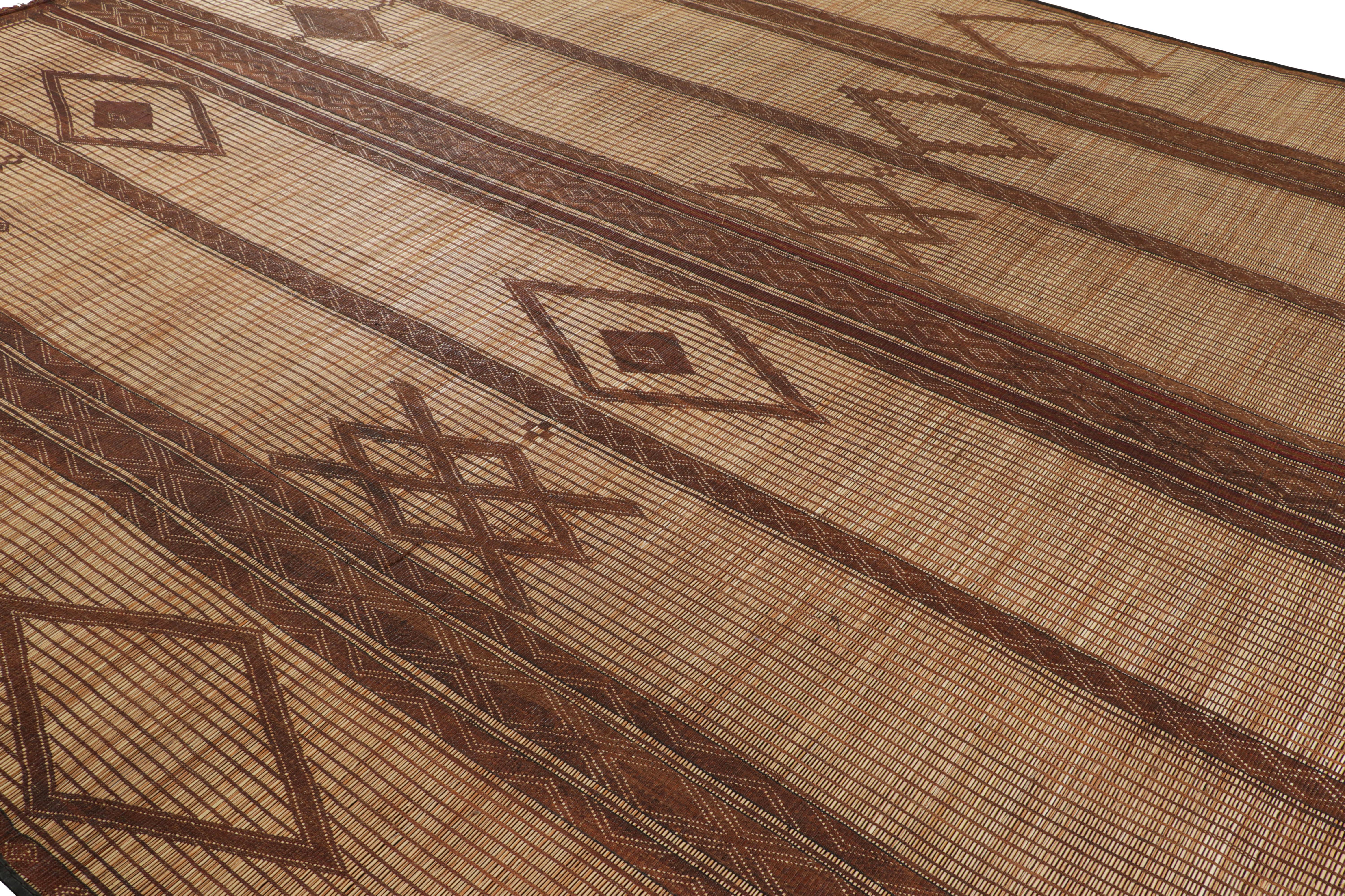 Questo pavimento marocchino vintage di grandi dimensioni è una stuoia Tuareg 11x16 dell'omonima tribù nomade. Intrecciata a mano con canne e pelle intorno al 1950-1960, i suoi materiali naturali si esprimono nei toni caldi del marrone e del beige