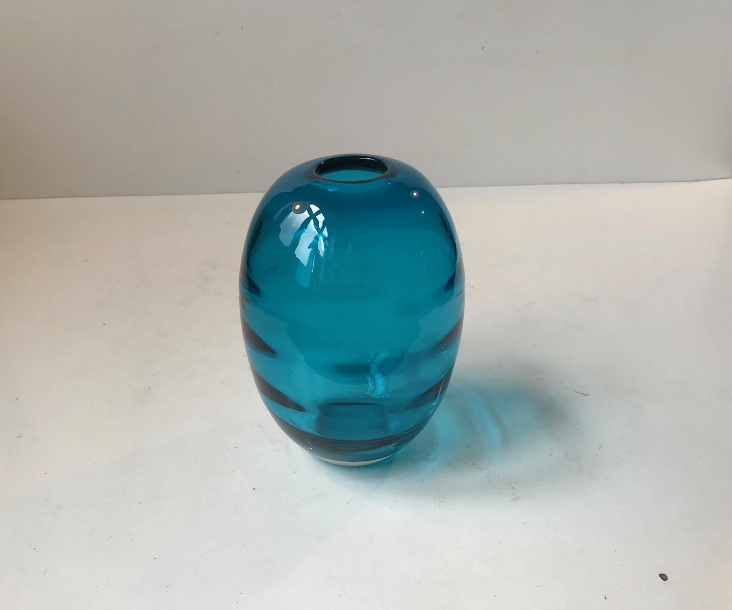 Vase en verre turquoise soufflé à la main, fabriqué par Holmegaard au Danemark dans les années 1950. Belle couleur turquoise profonde et décorée intérieurement de bandes optiques horizontales qui soulignent la forme ovoïde. Il ne porte pas de
