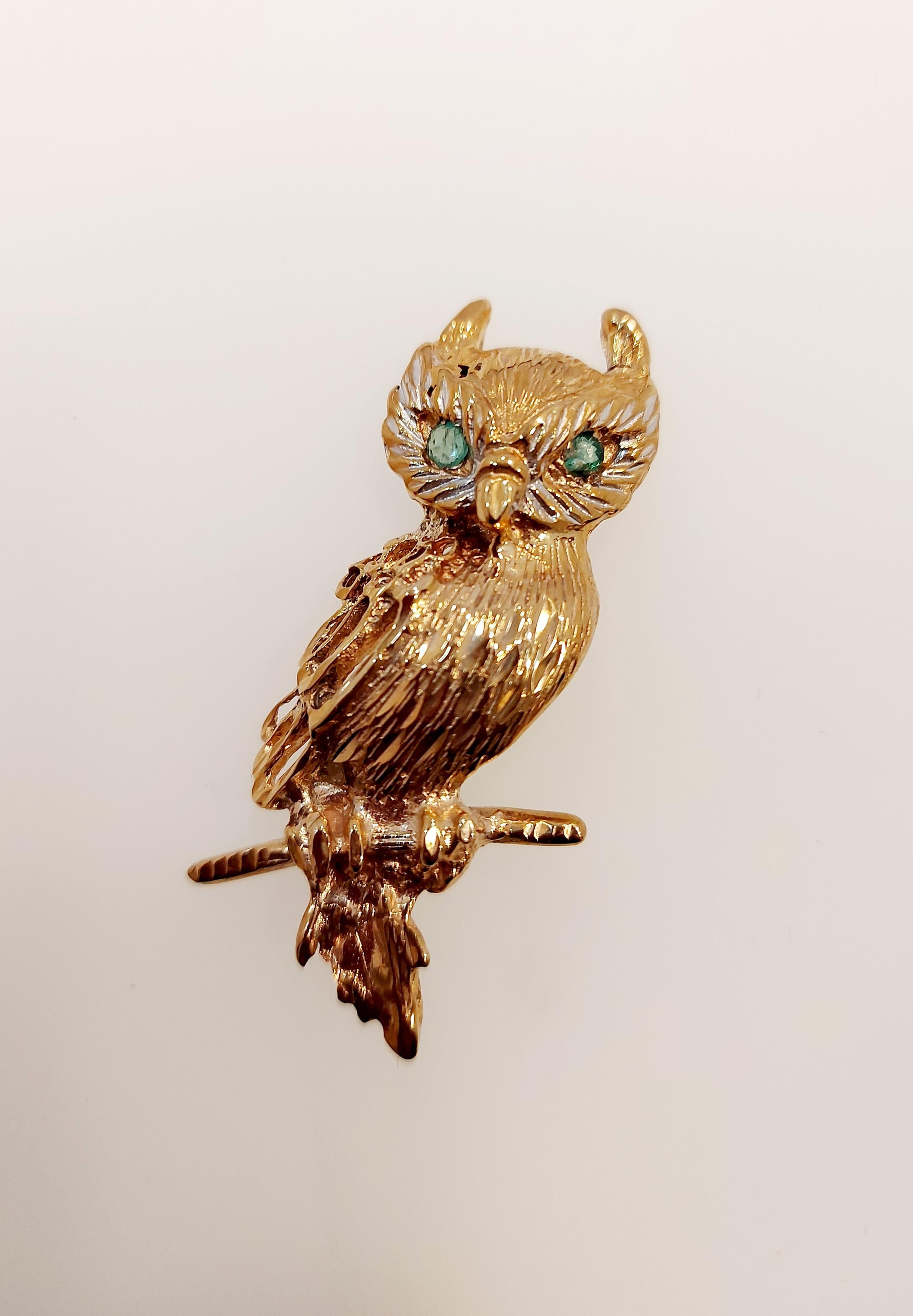 An owl brooch with emerald eyes hallmarked 9ct gold, textured feather detail perched on a gold branch. With pale green emerald eyes, assayed at Birmingham in 1989.