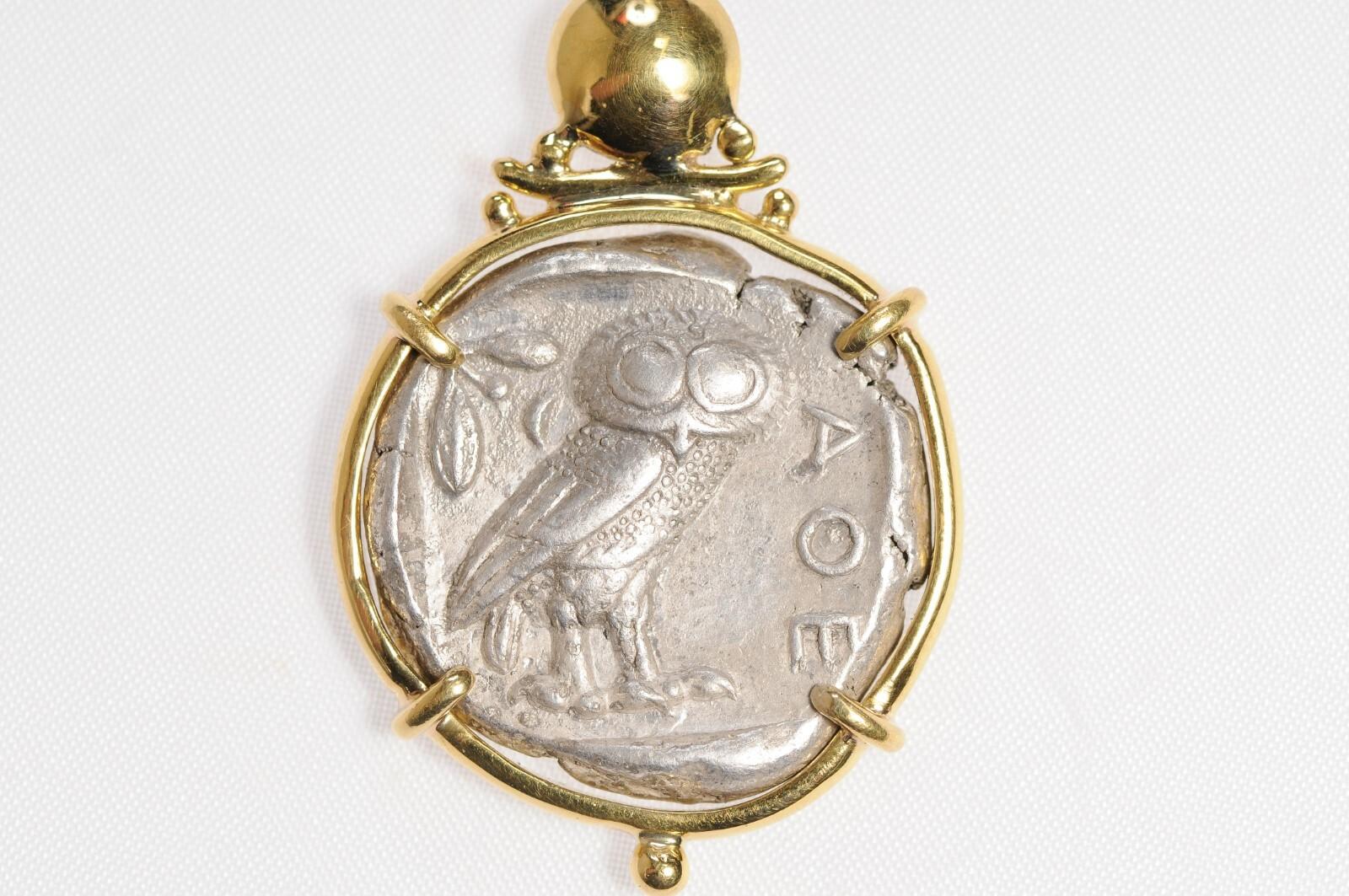 A silver Tetradrachm Owl pendant with Diamond accent and 22 kt gold surround. Decorative gold details add a beautiful touch to this already remarkable Tetradrachm piece. On the reverse side, there is an AOE and owl with an olive sprig and crescent