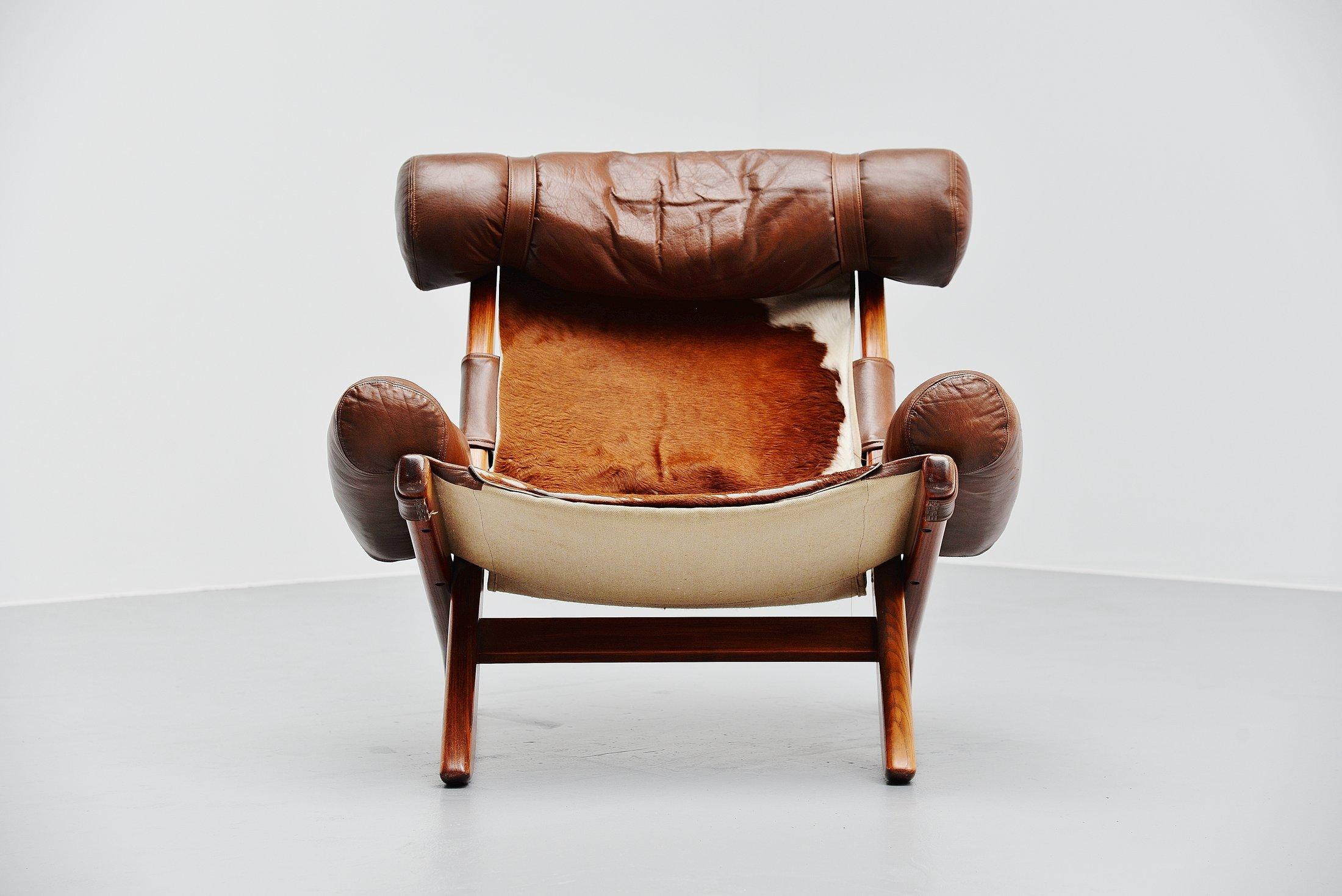 Very nice and unusual 'Ox' lounge chair attributed to Sergio Rodrigues, Brazil, 1960. The chair is made of stained teak wood and has cow skin leather seat supported with a canvas back and with brown leather arm rests and head cushion. The chair is