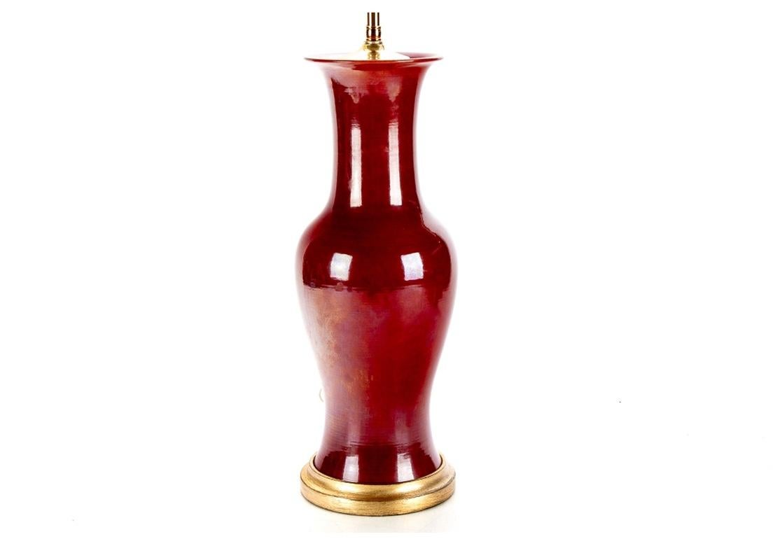 Sehr hochwertige, hochhalsige Vase im asiatischen Stil mit ochsenblutfarbener Glasur auf einem vergoldeten Holzsockel. Leviton-Doppel-Glühbirnenfassungen aus Messing und ein höhenverstellbarer gerippter Kugelabschluss. 
Maße: Höhe 28