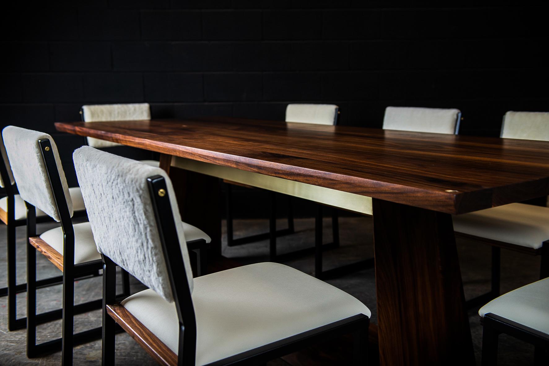 L'Oxford est une élégante table de salle à manger contemporaine fabriquée à la main sur commande à partir de bois dur américain massif sélectionné à la main, avec de subtils détails en laiton poli à la main. Tandis que l'élégante base centrale à