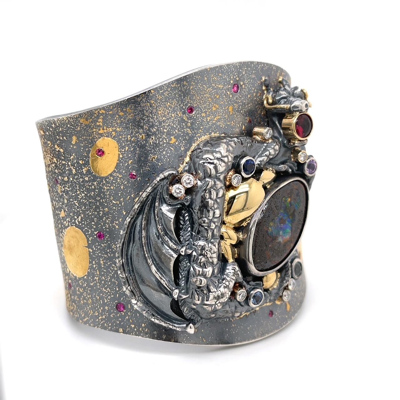 An oxidized sterling silver, 18k and 22k yellow gold dragon cuff set with one 14.46 carat oval boulder opal, .66 carats of round rubies, .21 carats of diamonds, .61 carats of blue, pink, and green sapphires, and one round .85 carat 5.5mm pyrope