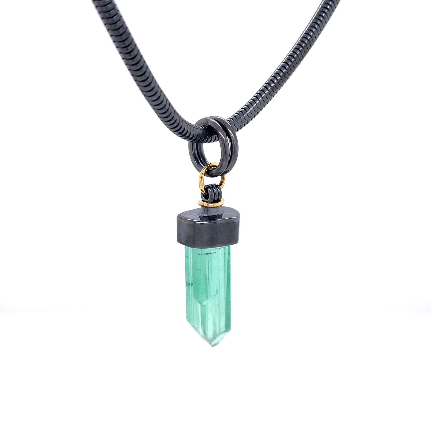 An oxidized sterling silver and 18k yellow gold pendant set with one 19.32 carat green tourmaline crystal on a 3mm 18 inch oxidized sterling silver snake chain. This necklace was made and designed by llyn strong.