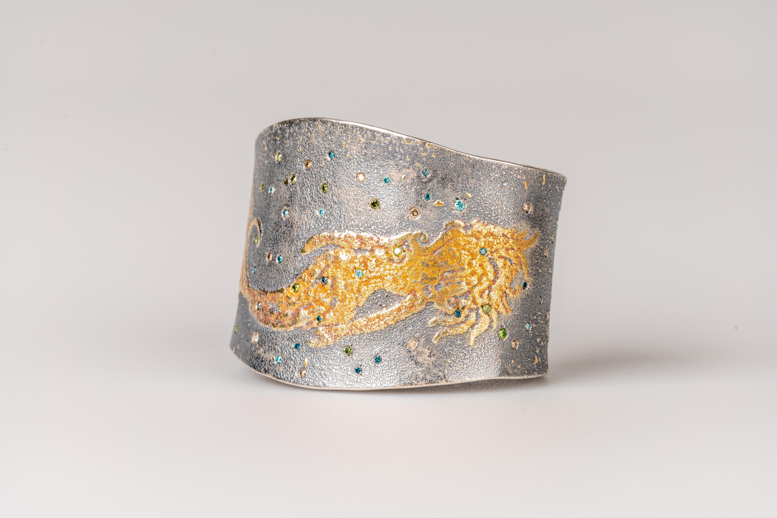 An oxidized sterling silver cuff with 24k gold mermaid design, 24k gold fairy dust, and 1.02total carat weight aqua blue, teal blue. green, and champagne flush-set diamonds, measures 2.20inches x 1.72inches inside. Made and designed by llyn