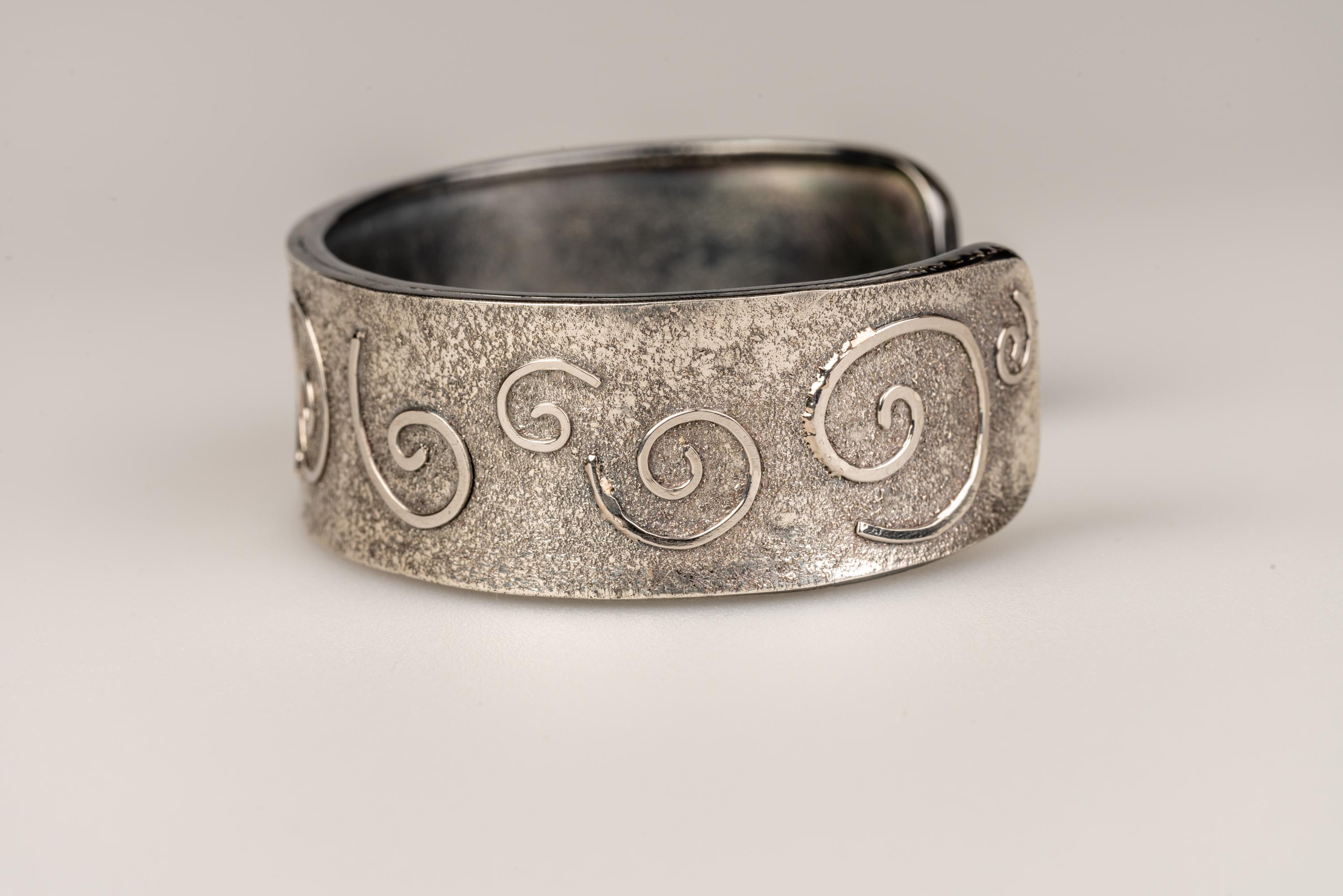 An oxidized sterling silver small swirly cuff with platinum dust and platinum wire fused to the surface. This cuff was made and designed by llyn strong.