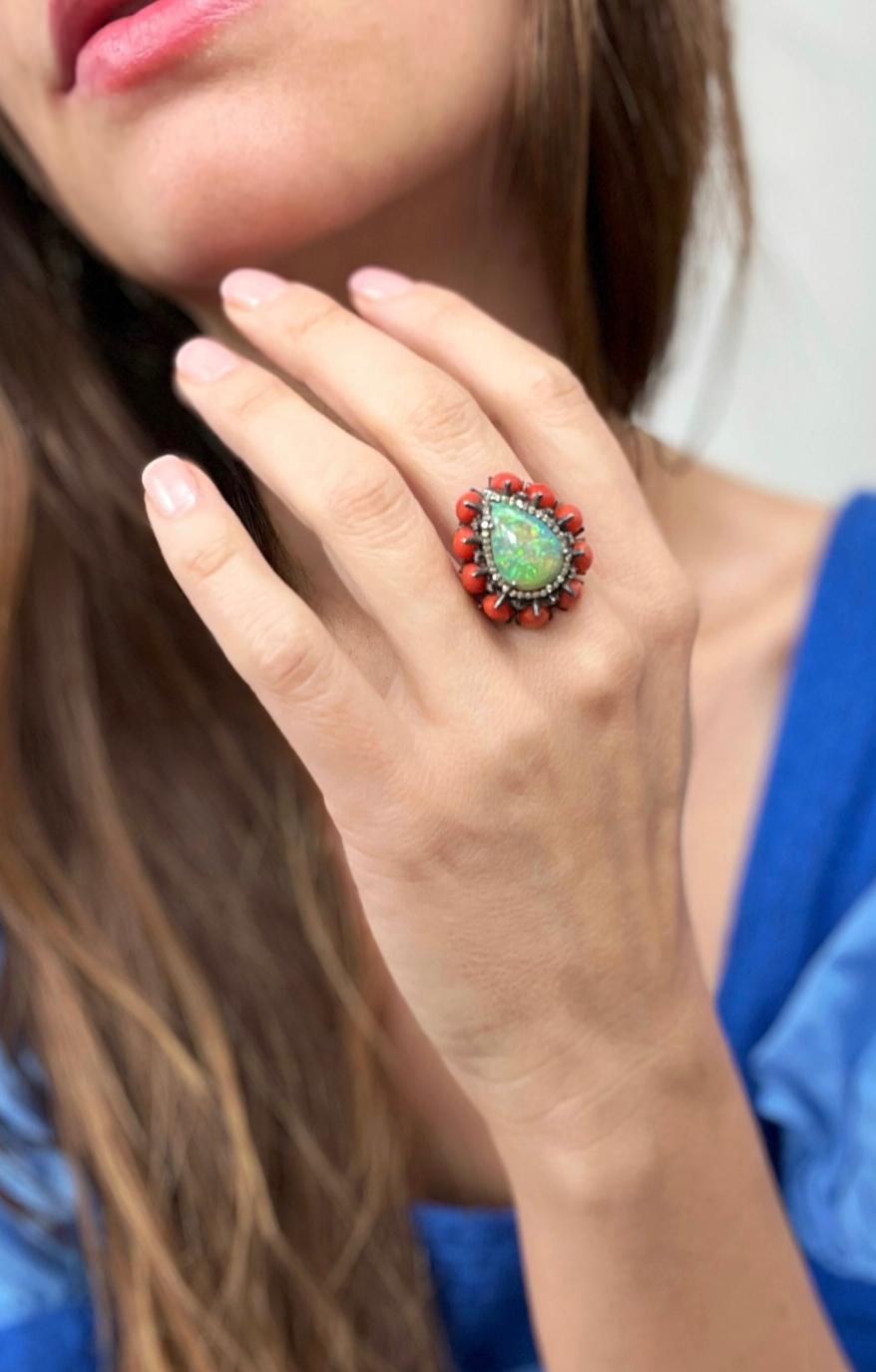 One oxidized sterling silver ring set with one 15x10.5 pear shaped Ethiopian opal, sixty-four round diamonds, approximately 0.58 carat total weight with matching I/J color and SI3 clarity, and ten 7x5mm pear shaped oxblood coral stones.  The ring is