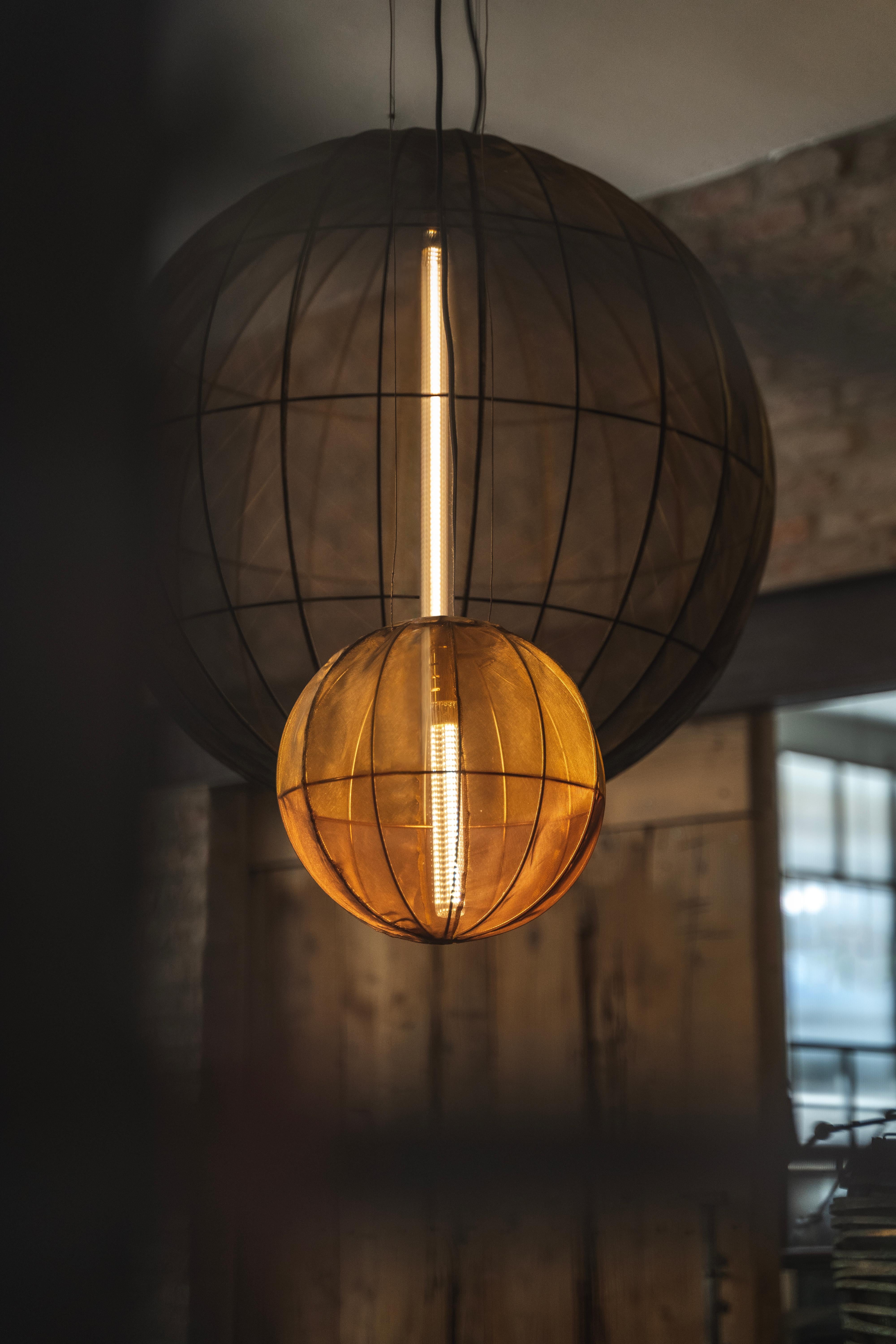 The Oxygen Spheres are a collection of light and graceful suspension lamps.Their structure is carefully wrapped with a metallic fabric, a work of high craftmanship.
These lamps are extremely light even in their largest versions and are therefore