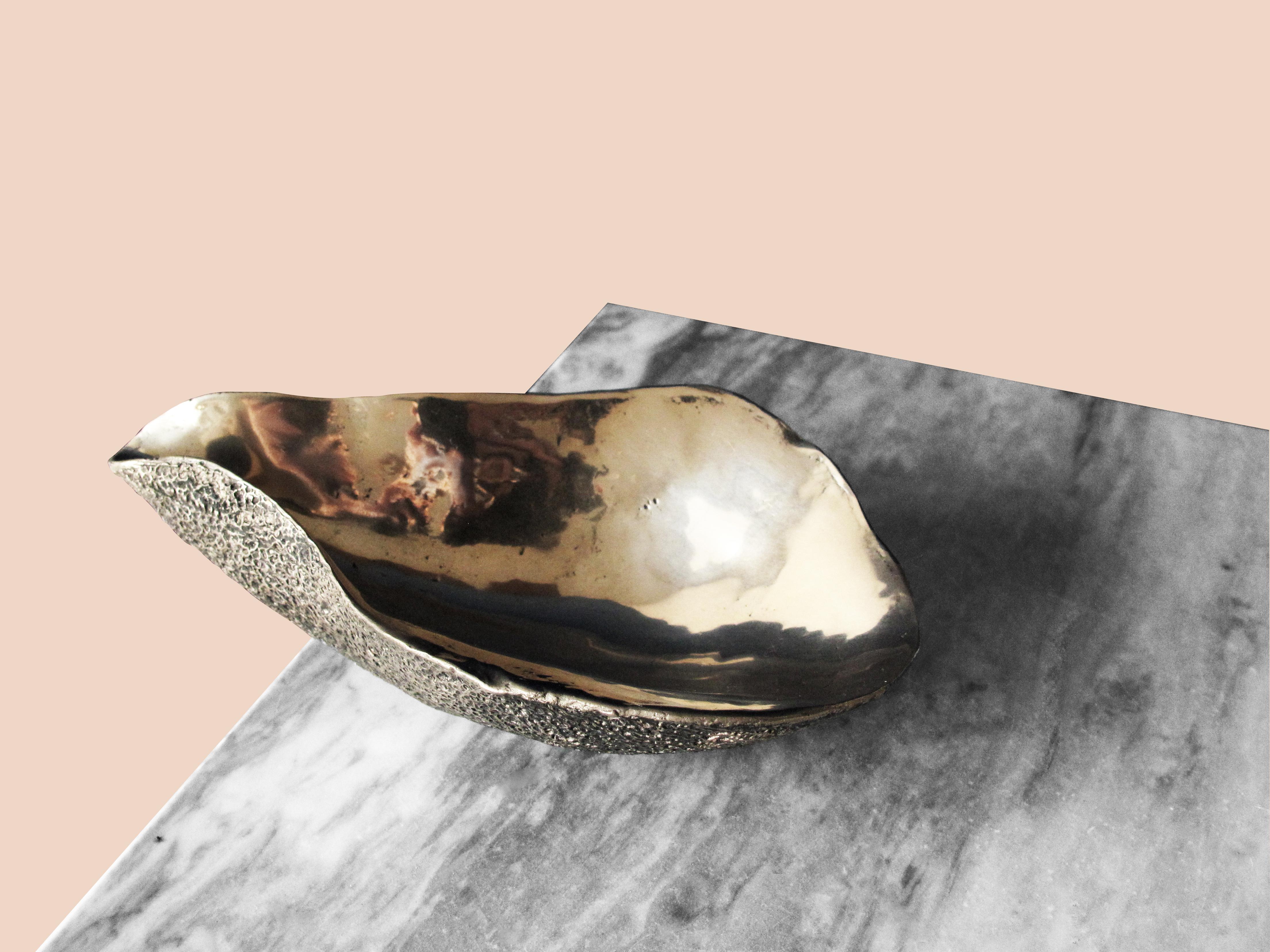 This solid bronze dish is an interior embellishment. 
The organic shape is sculpted by hand, richly textured on the outside and polished on the inside. Inspired by the feminine and evocative shapes of oyster shells, this home accessory will add a