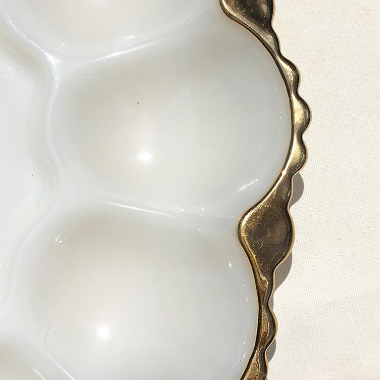This beautiful milk glass egg or muscle/oyster plate is a beautiful addition to any table. This plate features 12 egg or oyster wells. The perimeter of the piece is painted in gold. The bottom is decorated in an intricate pattern of reliefs