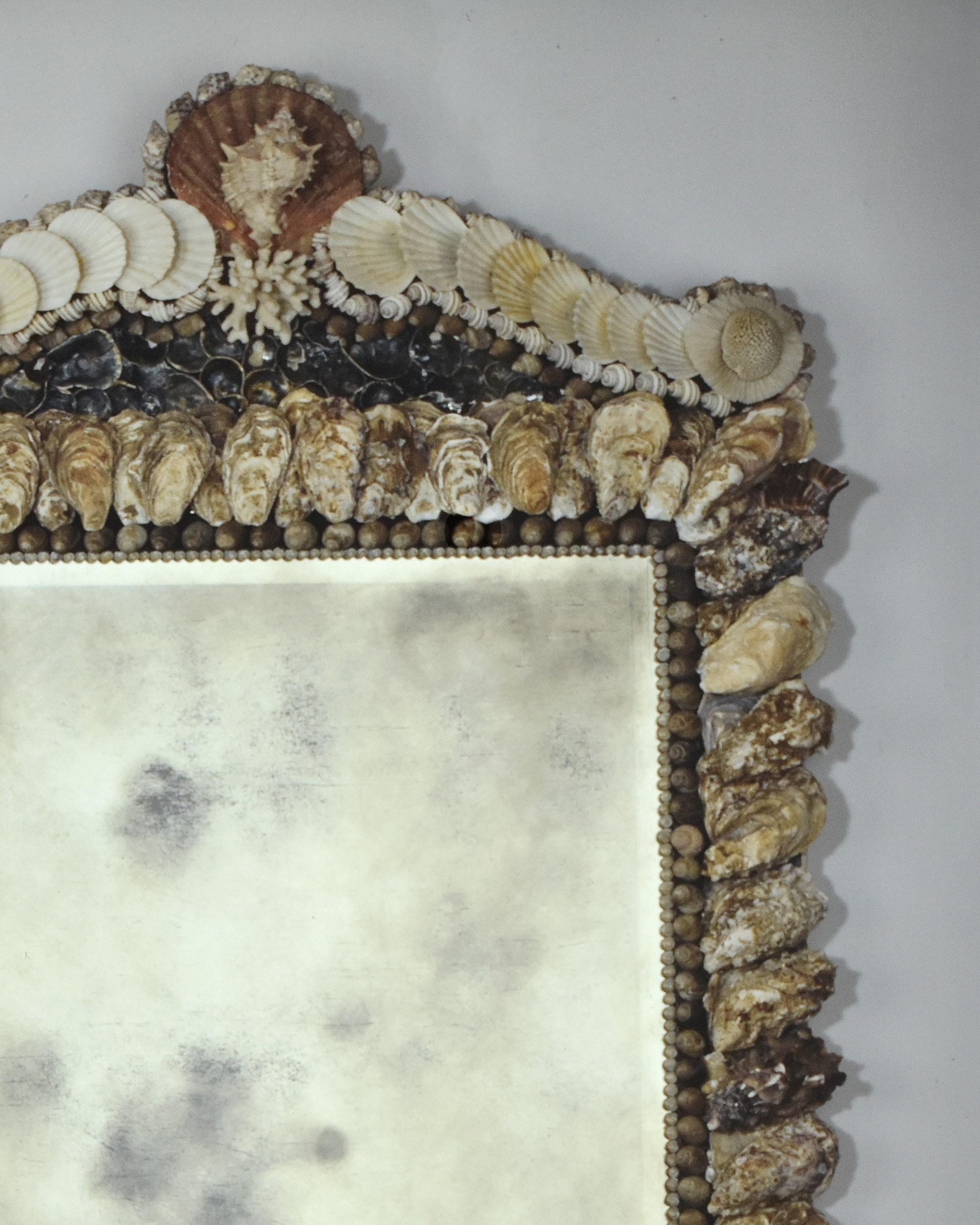 Un beau miroir rectangulaire incrusté de coquilles de bigorneaux et d'huîtres indigènes. Le fronton avec un fleuron en forme de coquille Saint-Jacques surmonté d'une seule coquille de murex et flanqué de volutes brisées d'éventails blancs et de