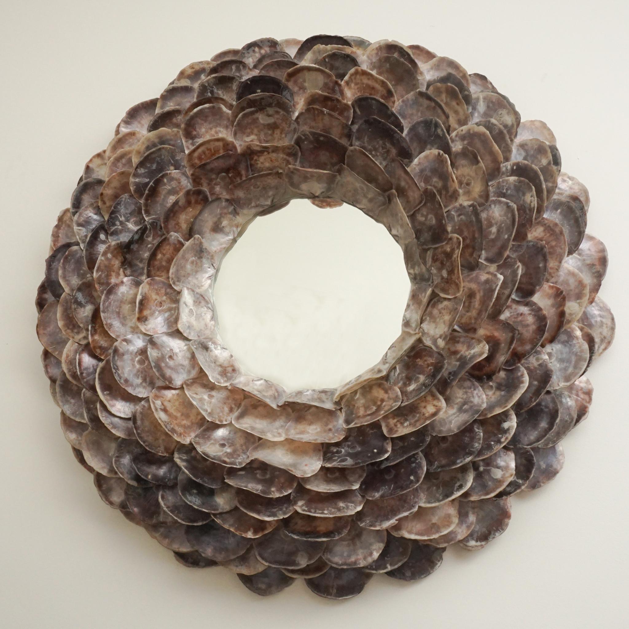 Le miroir rond spectaculaire, illustré ici, présente des coquilles d'huîtres disposées comme les pétales d'une fleur de 30 cm.  Les coquillages sont disposés de façon complexe, en tailles progressives, du plus petit au centre au plus grand sur le
