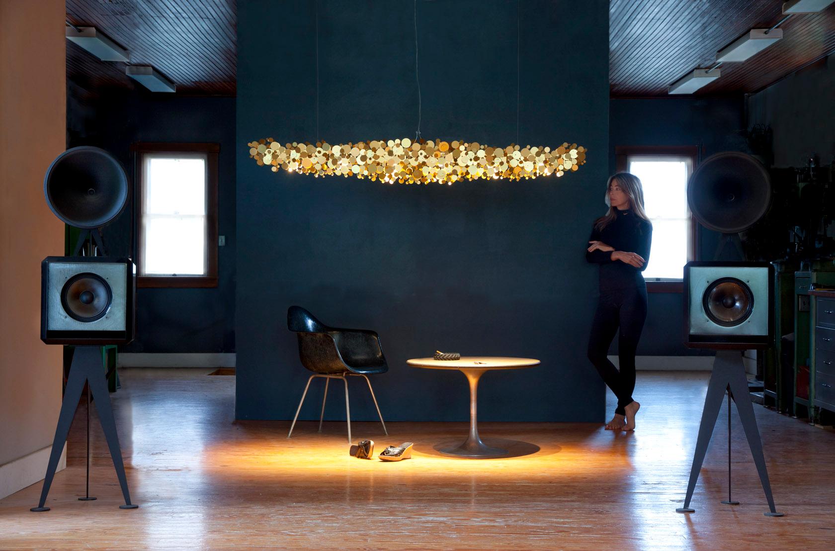 Ozone is a handmade gold anodized aluminum linear chandelier providing warm direct LED illumination when suspended over a dining table, kitchen island or conference table. Clusters of gold discs are arranged at different angles creating a surface of