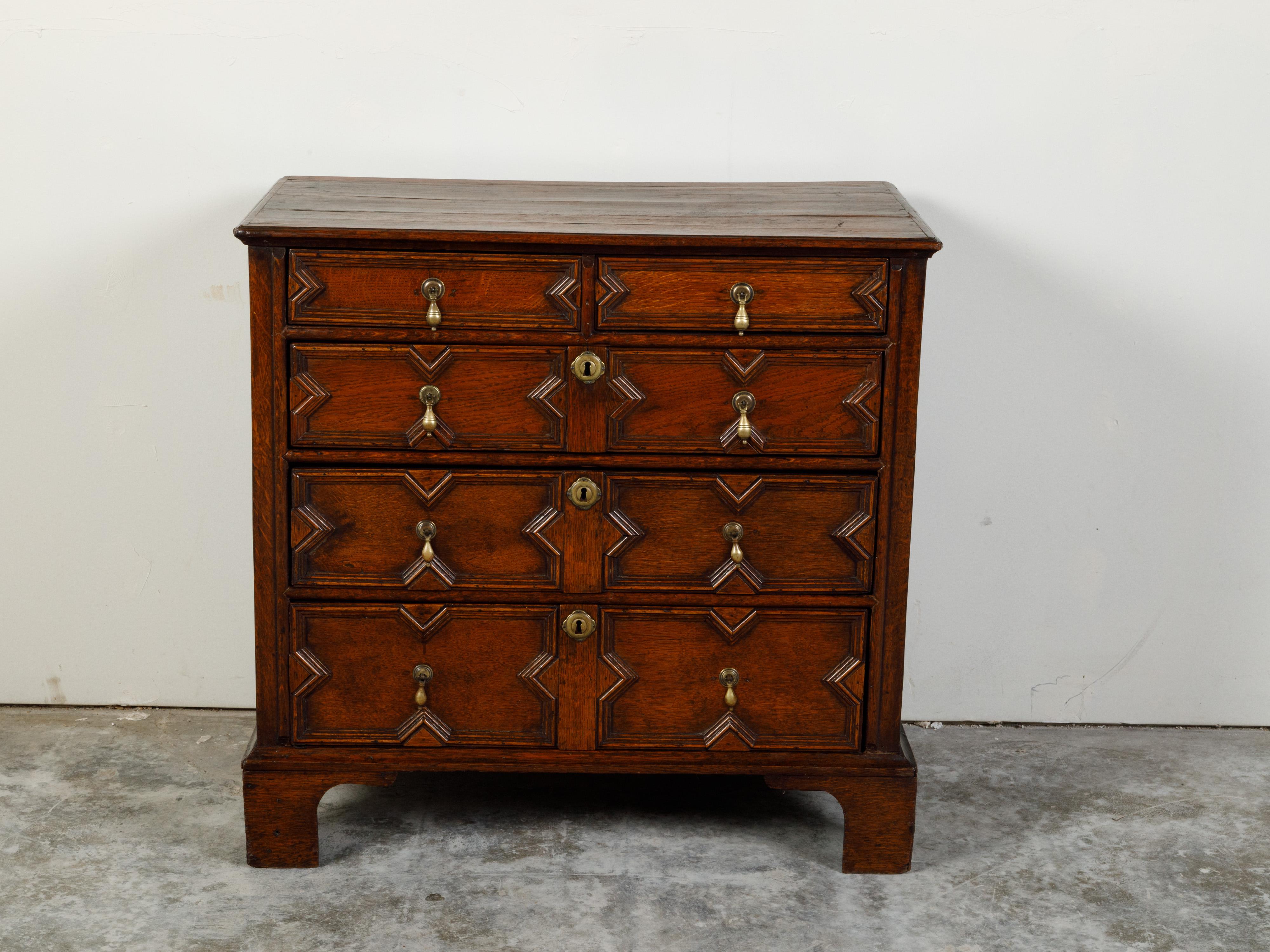 An English Georgian period oak geometric front five-drawer chest from the early 19th century, with bracket feet. Created in England during the early years of the 19th century, this Georgian chest features a rectangular planked top sitting above five