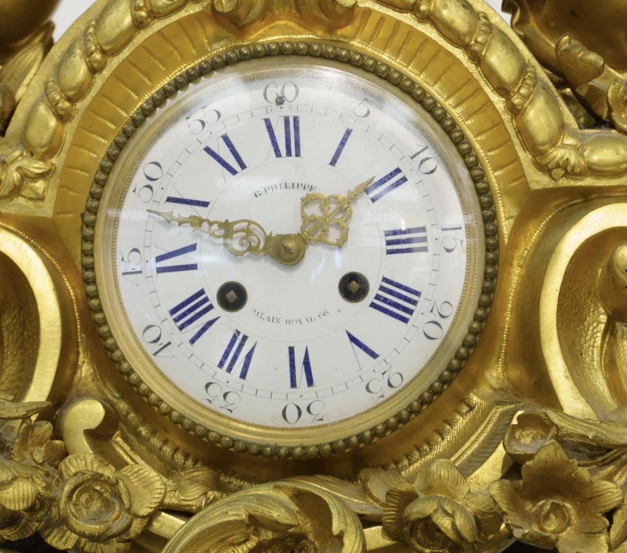 An ornate rocaille scrolled base with garland swags, centered the enamel white clock face with Roman and Arabic Numerals, the face with, G. Philippe, Palais Royal 66, flanked by two putto's holding a urn filled with flowers,

the mechanism stamped