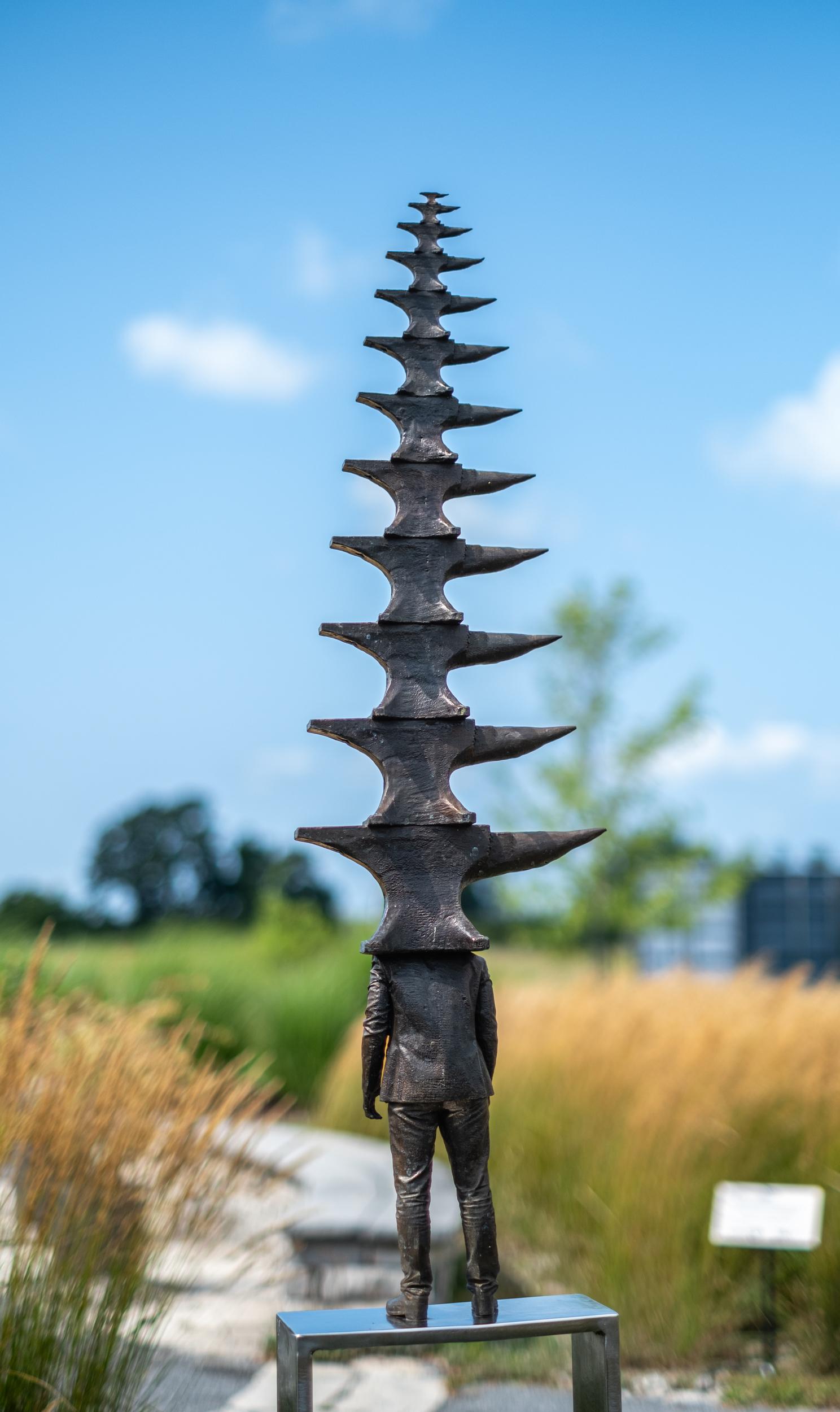 Esta escultura figurativa de bronce para exteriores es obra de Roch Smith. Inspirado por las grandes preguntas de la vida, Roch Smith crea esculturas contemporáneas reflexivas y lúdicas. Esta figura fundida en bronce y vestida formalmente con un