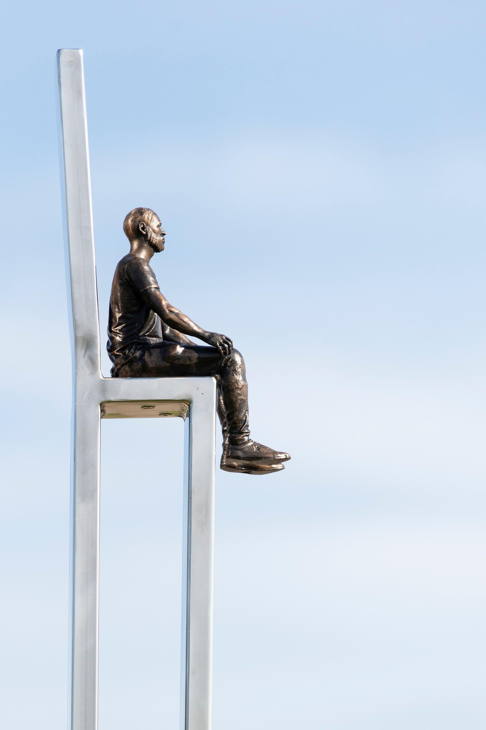 In this playful and imaginative sculpture by Roch Smith a figure, cast in bronze sits on a high steel chair. The Canadian artist is known for his inspired sculptures that often tackle the big questions in life in a fun way. The scale of the small