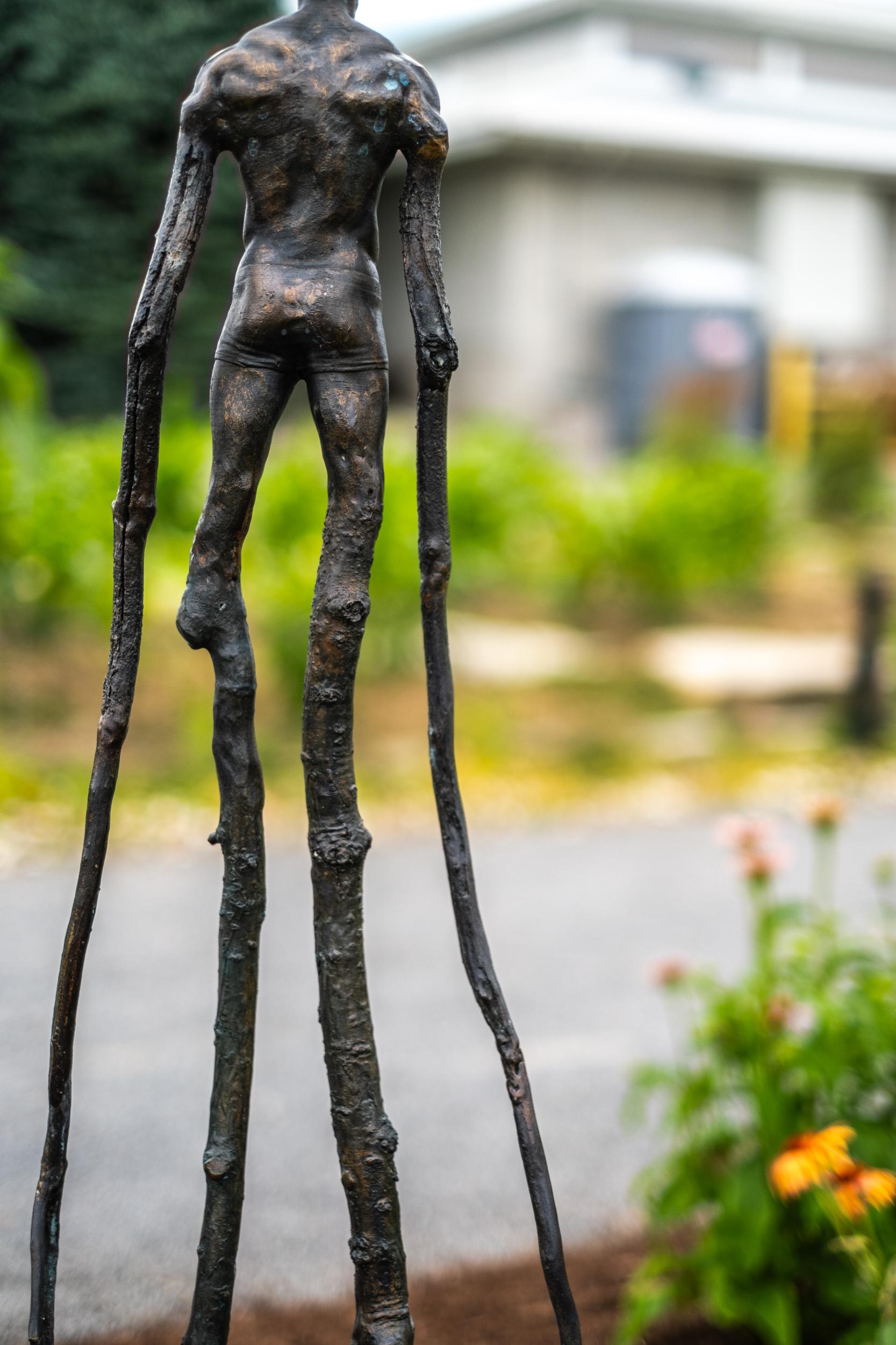 This surrealist, contemporary, figurative, bronze, outdoor sculpture is by Canadian sculptor Roch Smith. Smith returns to a favorite theme and form with this new imaginative ‘tree branch’ sculpture. Cast in bronze, the male figure (fit, shirt-free,