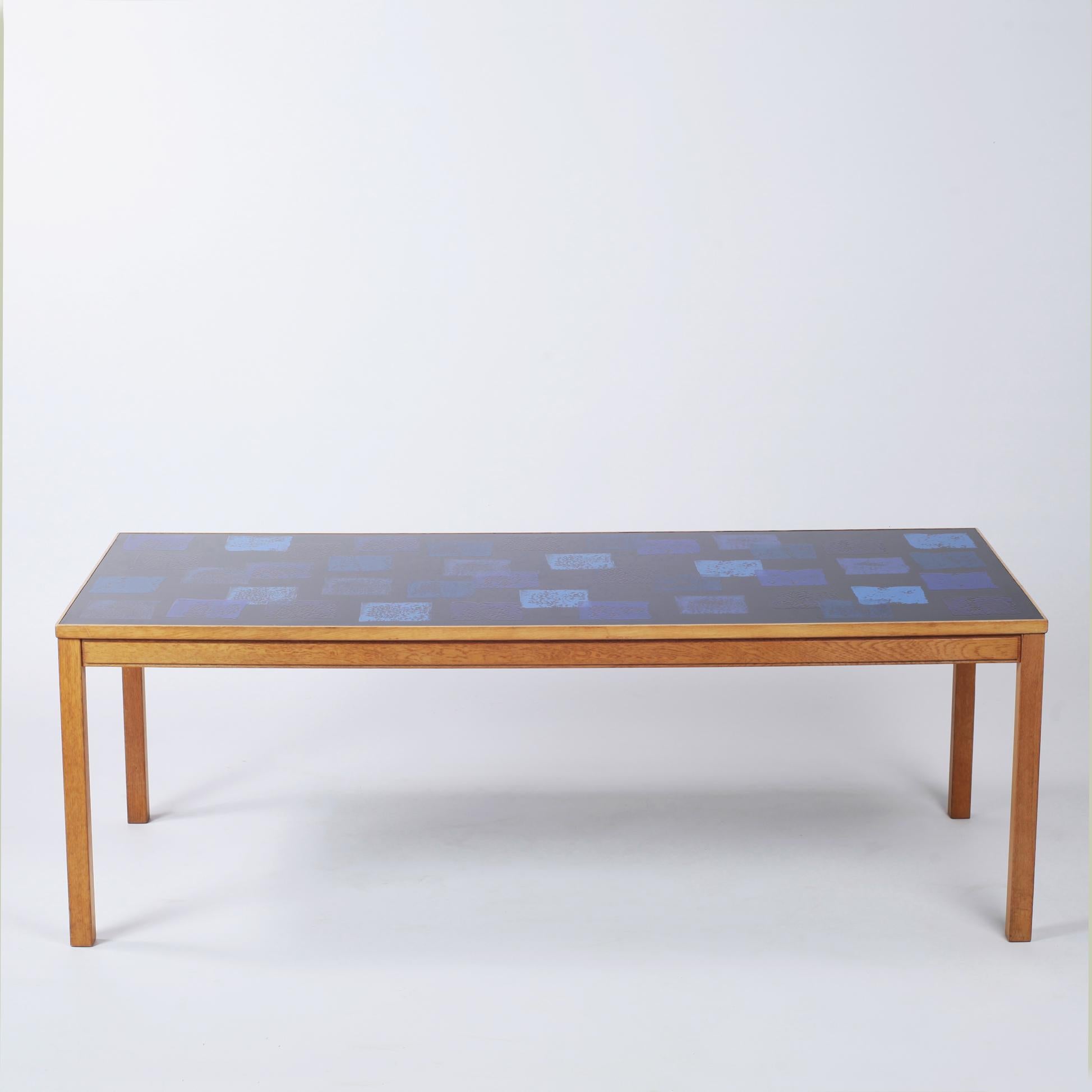 Swedish coffee table was designed by Algot P. Torneman and David Rosen for Nordiska Kompaniet during the 1960s. The oak structure supports an enamel top that is patterns with blue squares on a black background. The manufacturers label features on