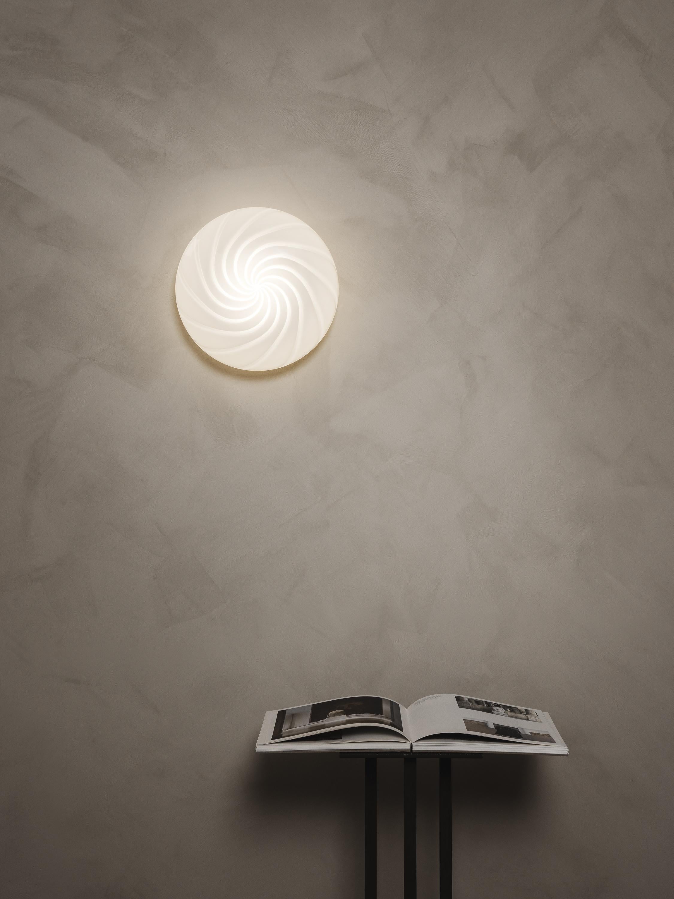 Defined by its curved mouth-blown opaline glass shade, this flush mount plafond lamp can be fixed on a wall or ceiling through a fitted hand-casted solid brass mount. The design features a swirl pattern obtained using an original 1970s mould,