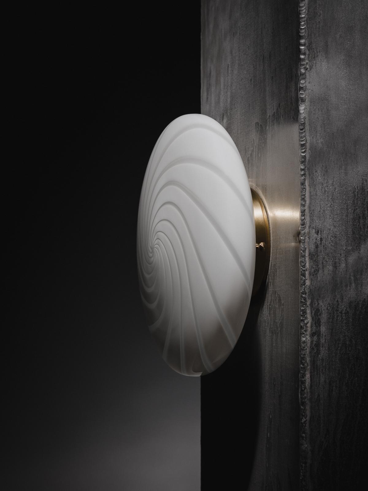 Defined by its curved mouth-blown opaline glass shade, this flush mount plafond lamp can be fixed on a wall or ceiling through a fitted hand-casted solid brass mount. The design features a swirl pattern obtained using an original 1970s mould,