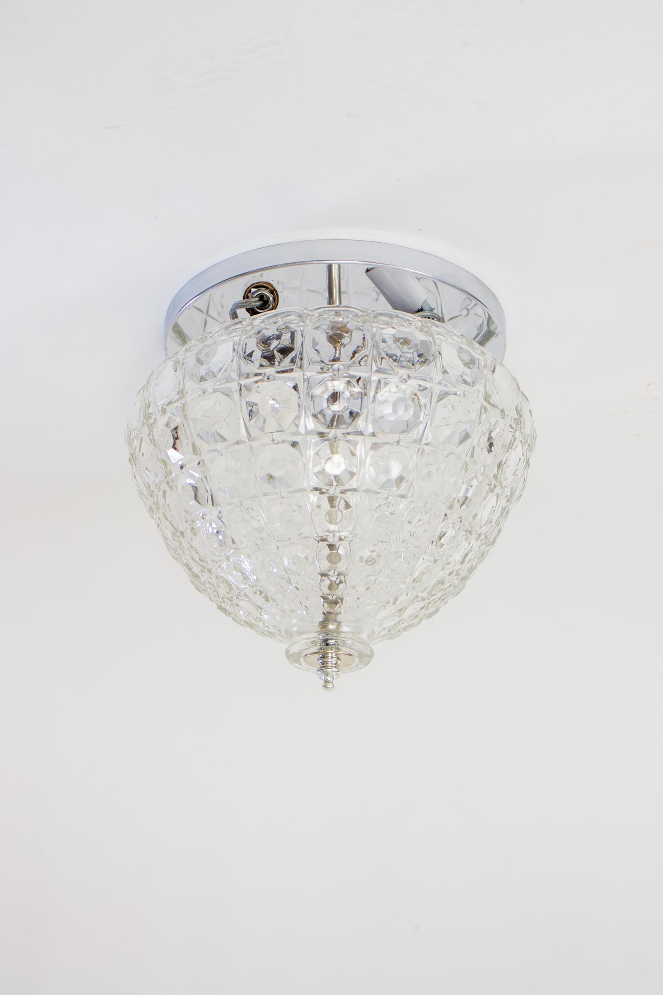 Mid-20th century crystalline glass flush mount fixture with chrome ceiling plate and three lights. A single clear glass dome, shaped to resemble a crystal basket. Silver colored hardware disappears to highlight the crystal. The sockets are
