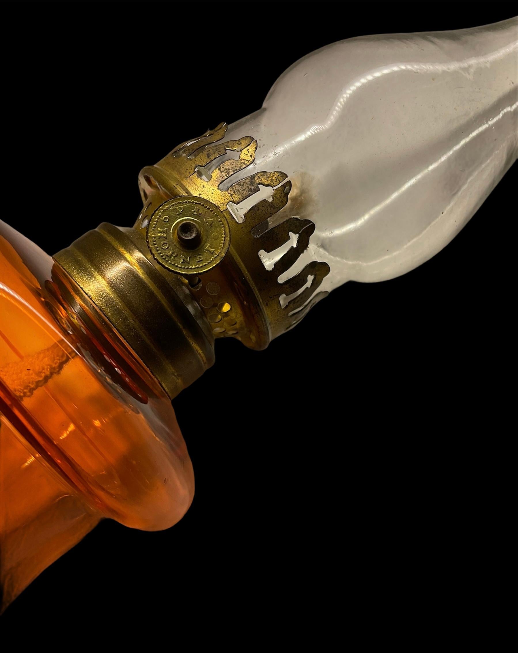 This a P&A Hornet small clear and orange glass kerosene oil hurricane lamp. It has a wick raising knob (the name of the company is inscribed on it) in one of the lateral aspect of the center of the lamp.
