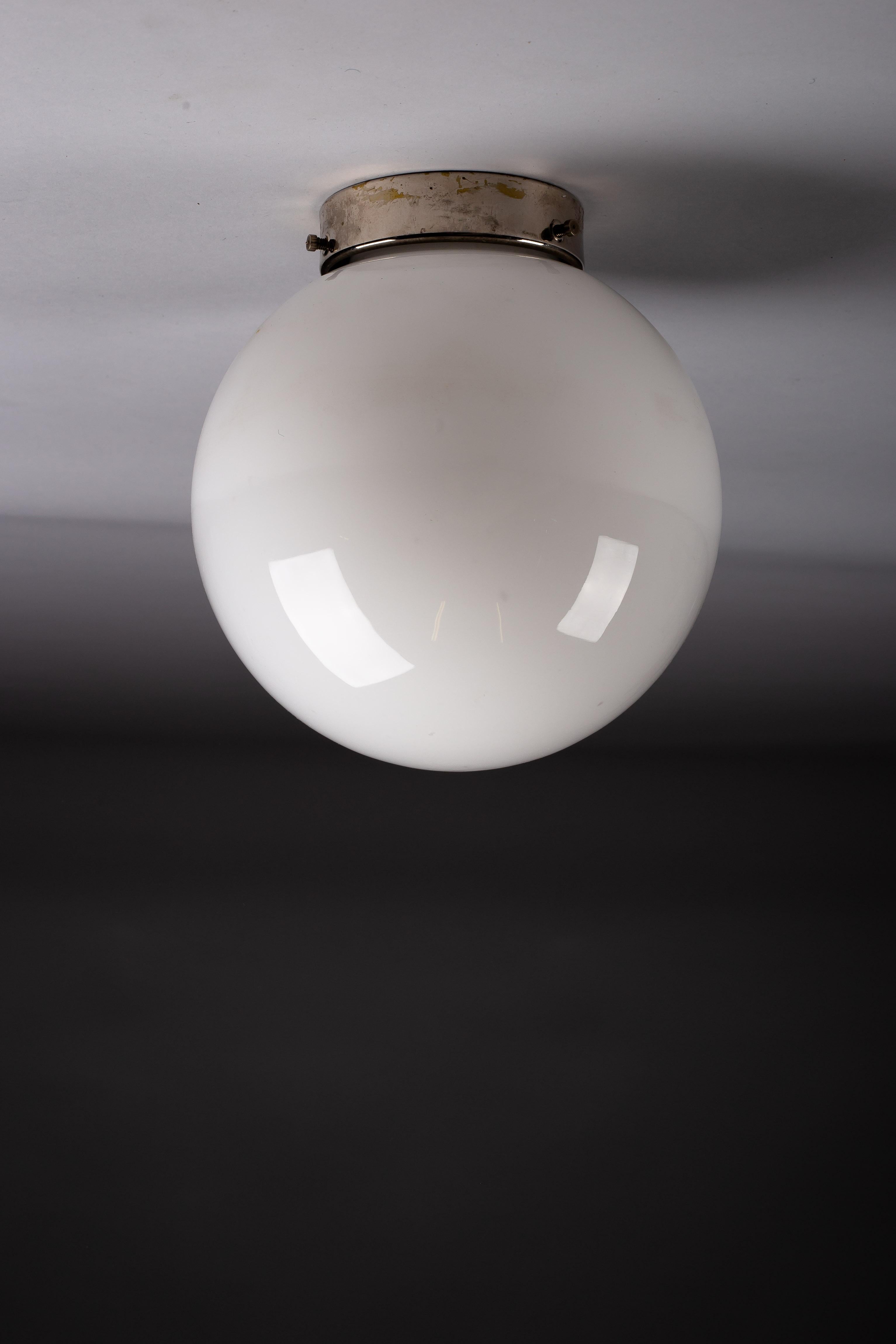 Illuminate your home with timeless elegance using this c. 1940's flush mount by renowned designer Paavo Tynell, crafted by Idman Oy, Finland. This opaline glass sphere flush mounts is perfect for your ceiling or wall, breathing classic Scandinavian
