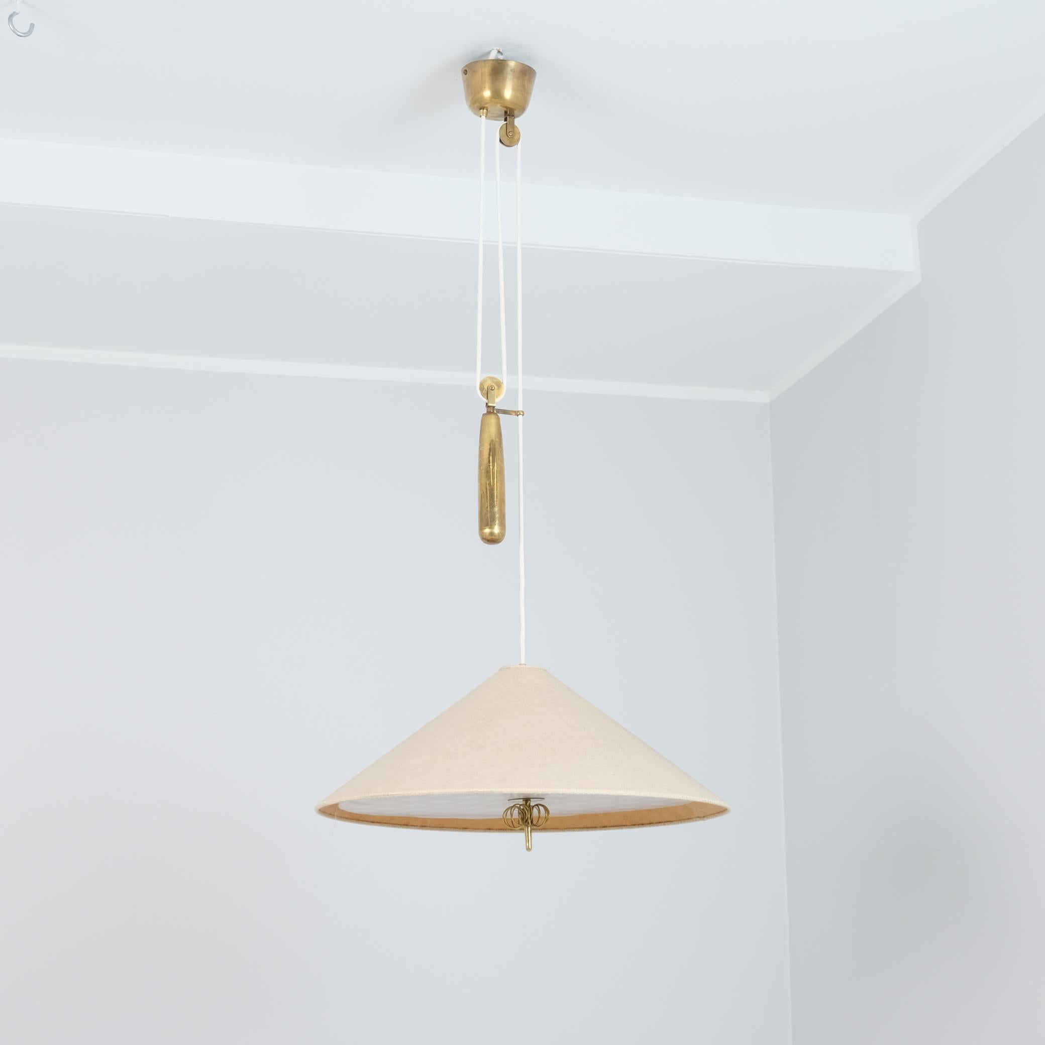 A beautiful adjustable ceiling pendant model 1967 by Paavo Tynell that harmoniously unites the patinated brass with the original linen shade and polka doted diffuser. The counterweight showcases Tynells genius by making the lamp suitable for