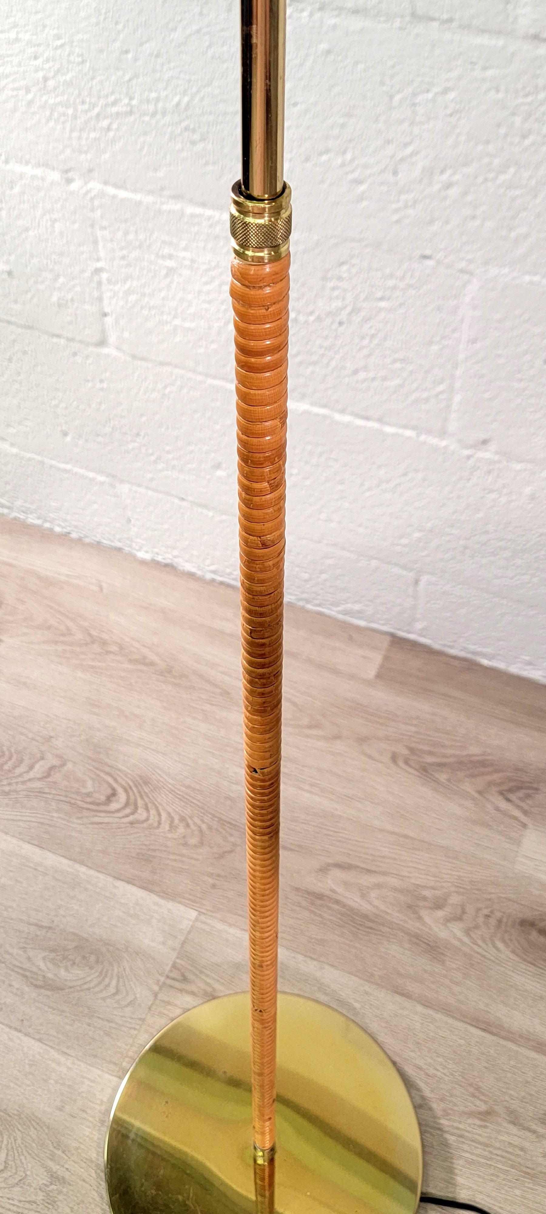 Vintage polished brass and rattan articulating floor lamp. The adjustable floor lamp features: rattan wrapped pole; pivoting or swing arm; brass shade; and a round, brass base.