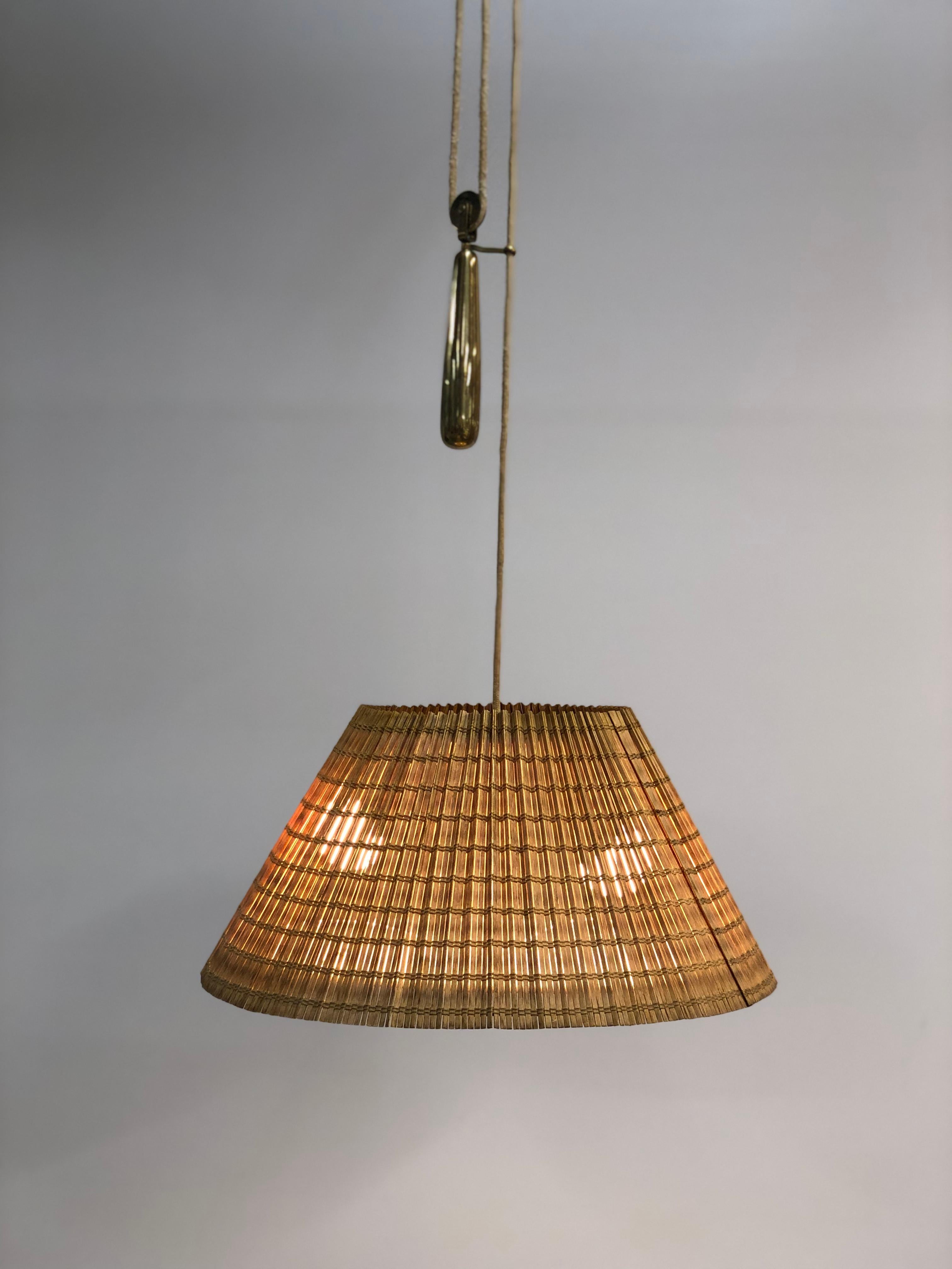Eine schöne verstellbare Lampe von Paavo Tynell, die das patinierte Messing harmonisch mit dem Rattan und dem Stoffschirm verbindet. Das Gegengewicht zeigt Tynells Genialität, indem es die Leuchte für verschiedene Deckenhöhen geeignet macht. Die