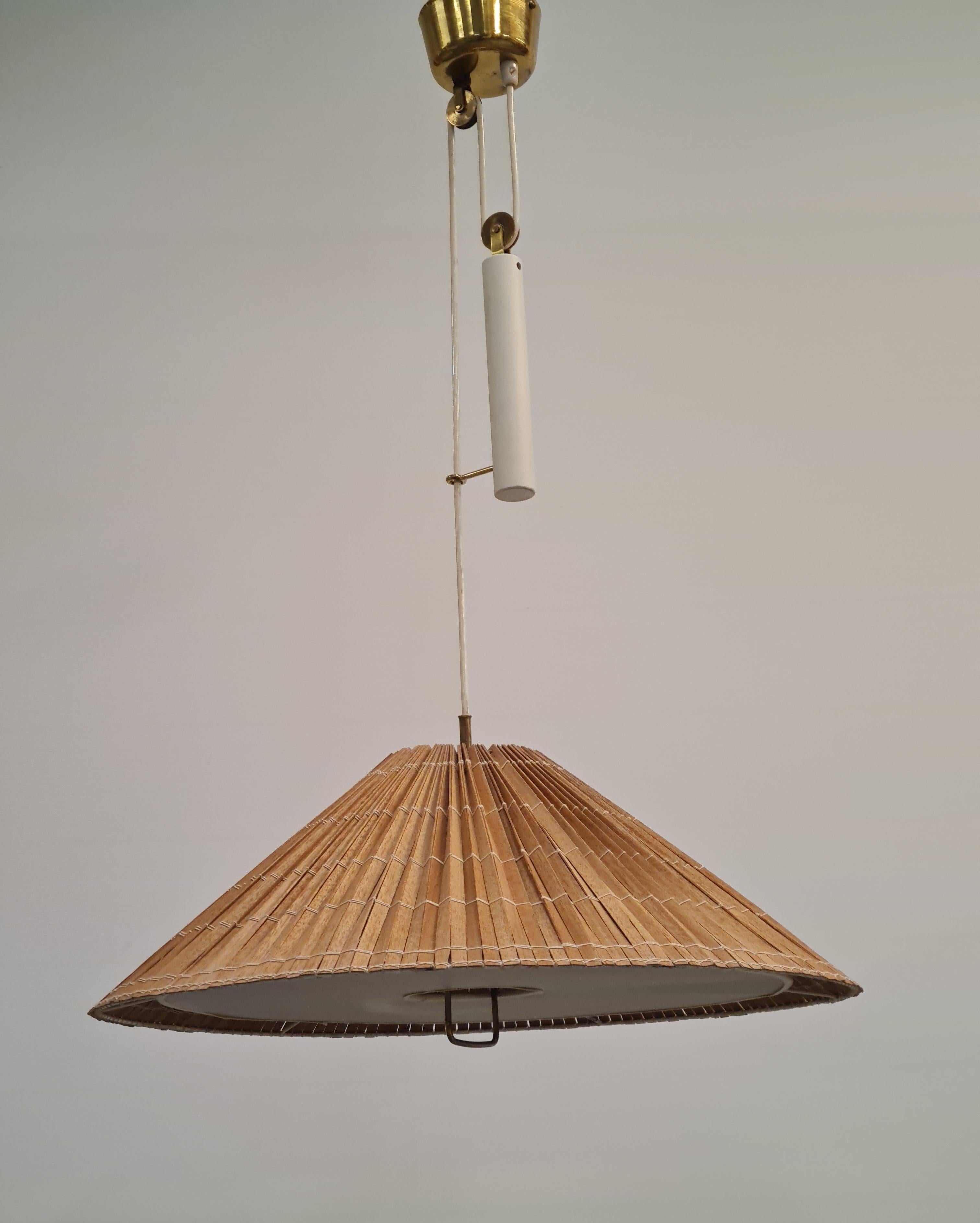 A beautiful adjustable lamp by Paavo Tynell that harmoniously combines many elements such as brass, wooden slats, plastic defuser, painted metal and the wirings. 
The lamp has all original parts except for the renewed wooden slat shade that was